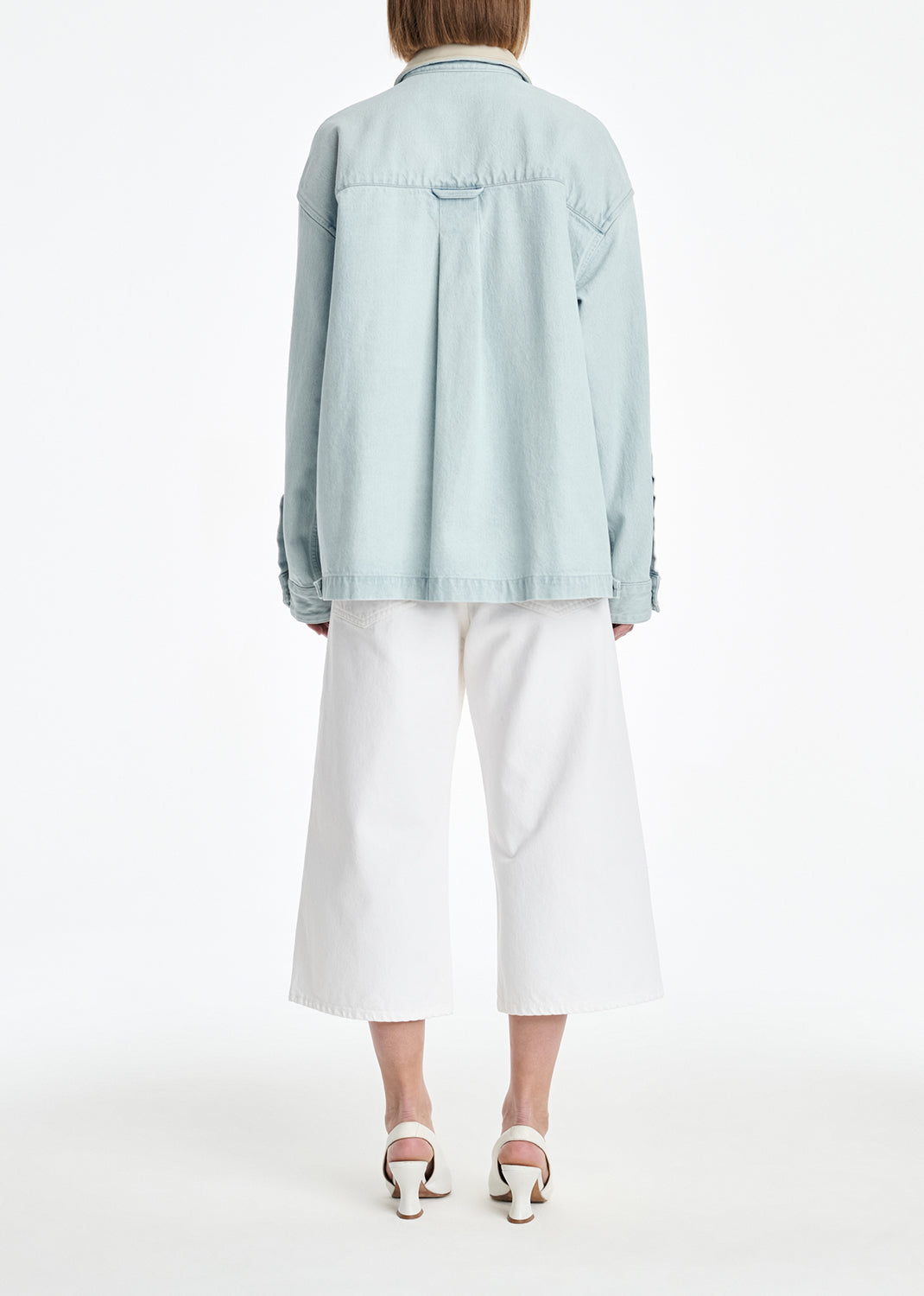 Person wearing a light blue denim jacket and white pants on a white background