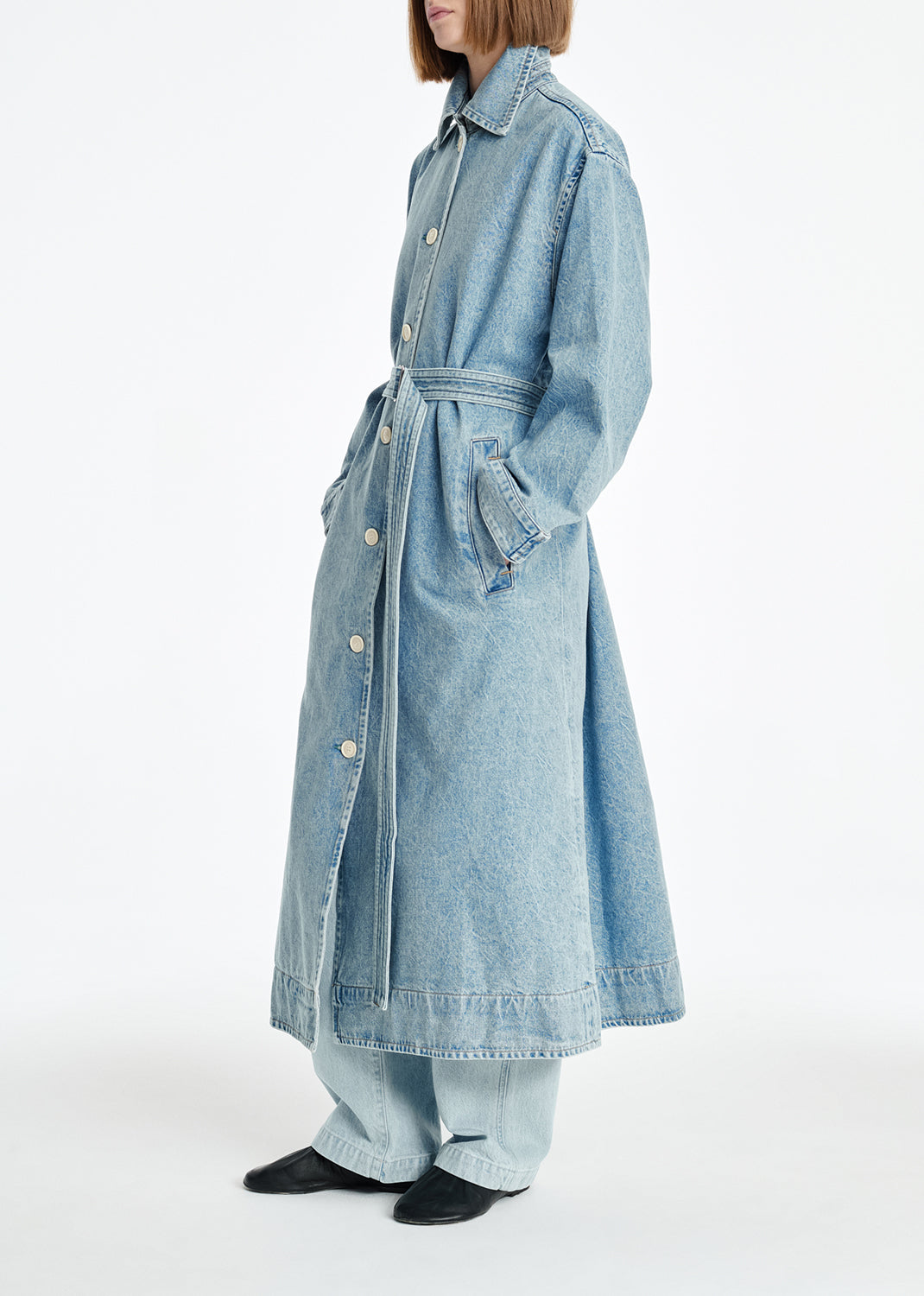Person wearing a light blue denim coat on a white background