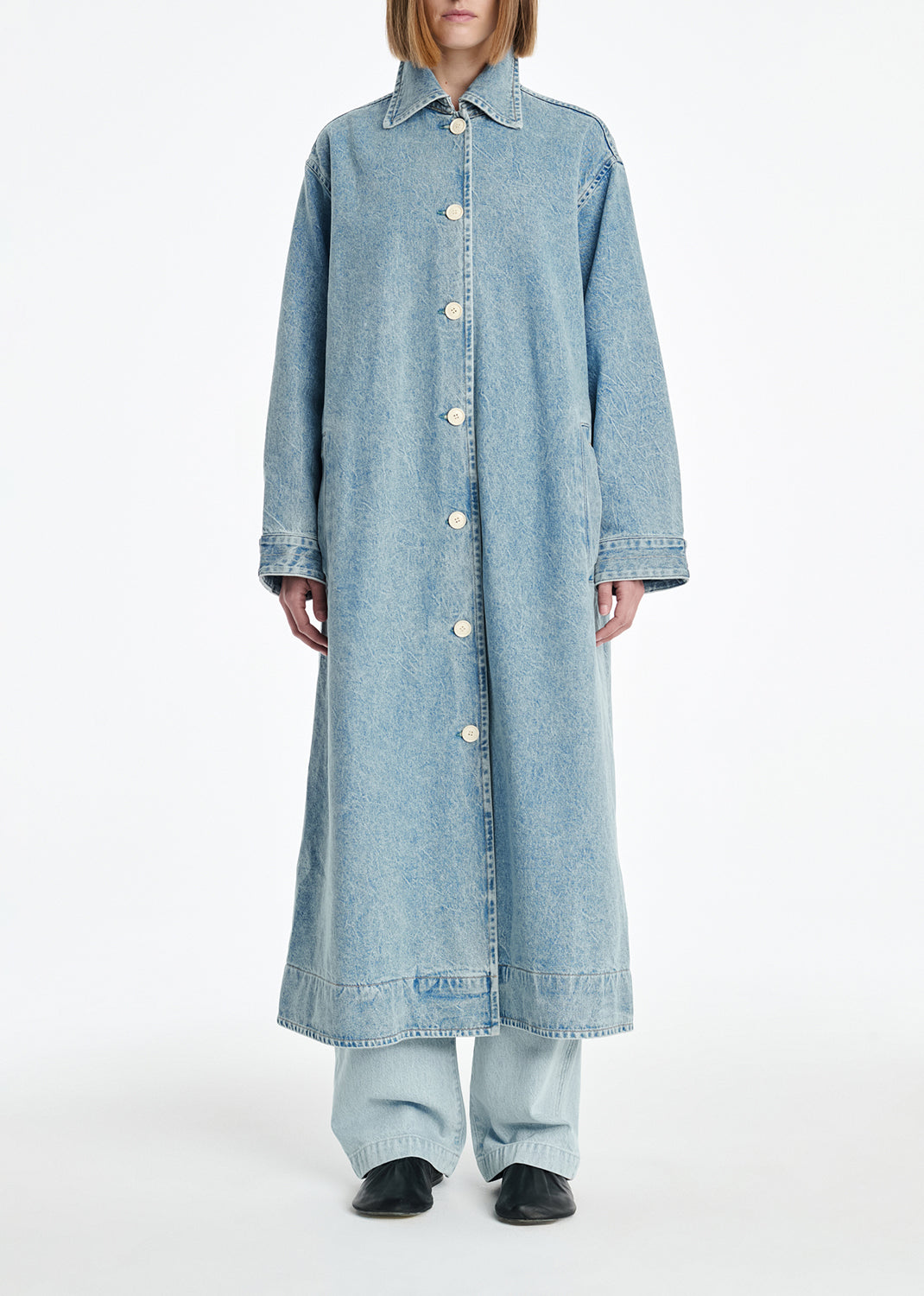 Person wearing a long denim coat on a white background