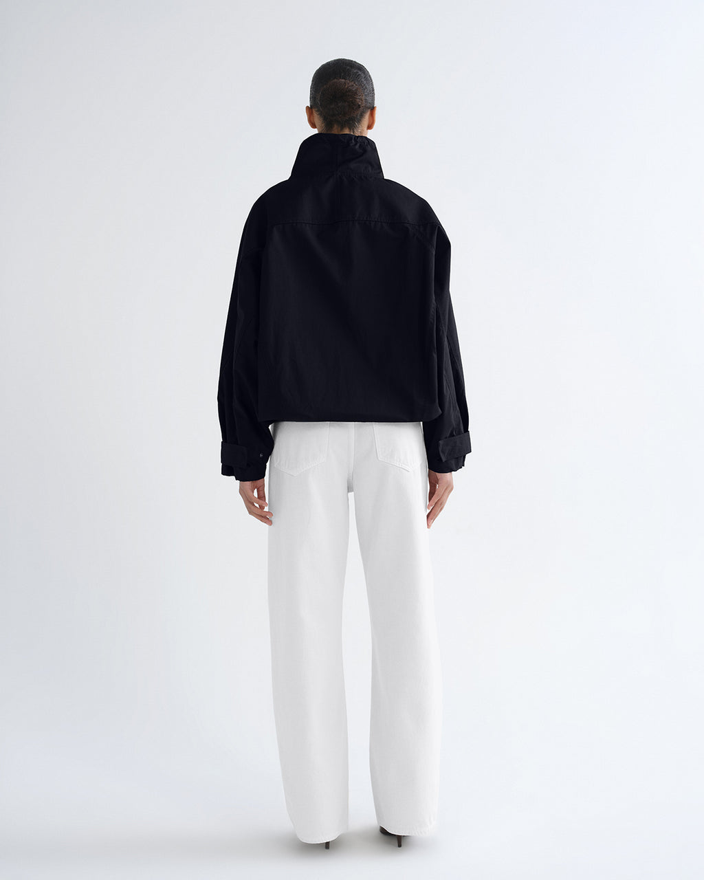 A model shown from the back wearing a black cropped jacket and white wide-leg trousers against a clean white studio background.