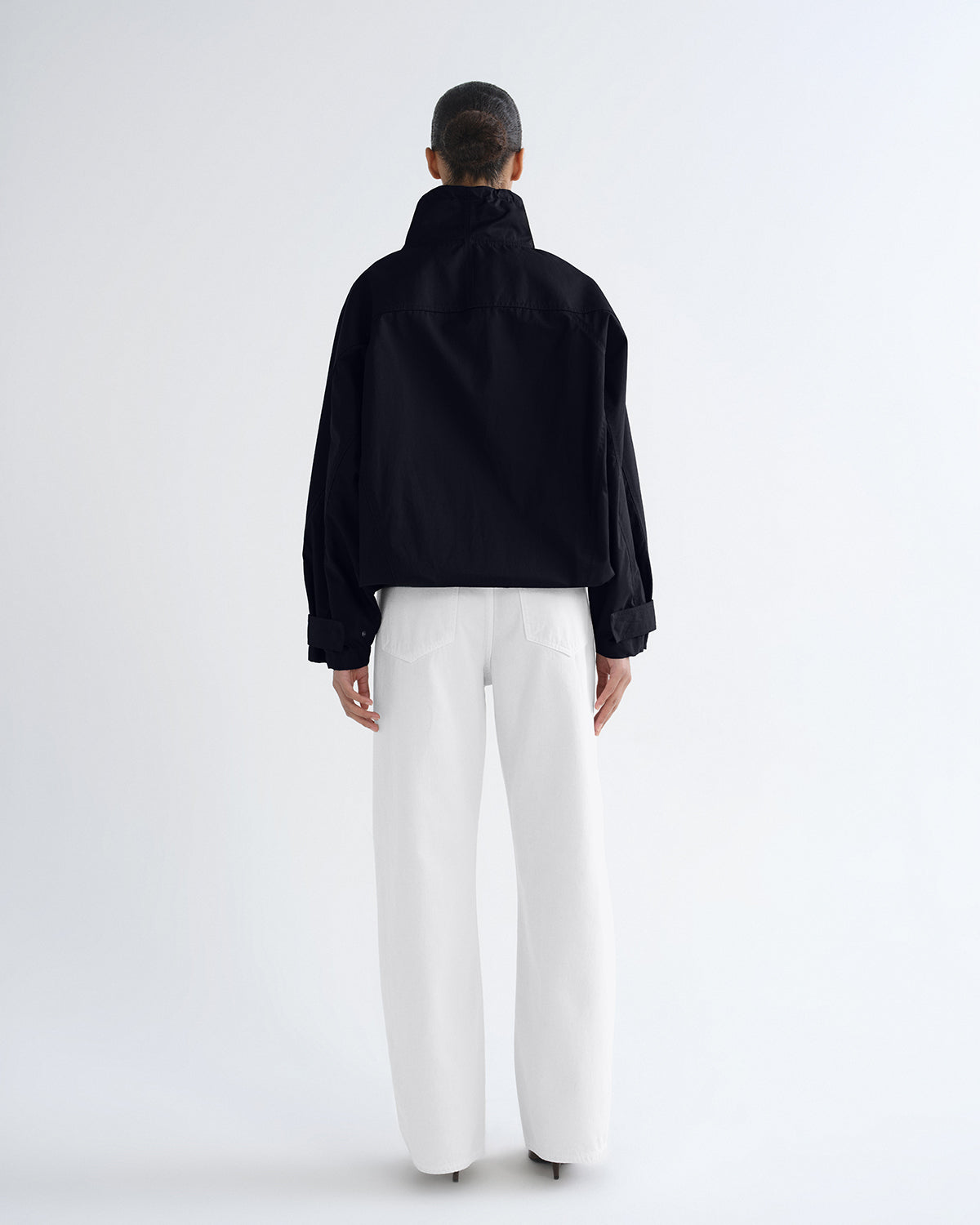 A model shown from the back wearing a black cropped jacket and white wide-leg trousers against a clean white studio background.