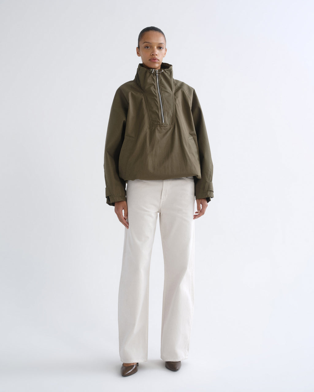 Person wearing olive green hooded pullover jacket and white pants, alternate front view
