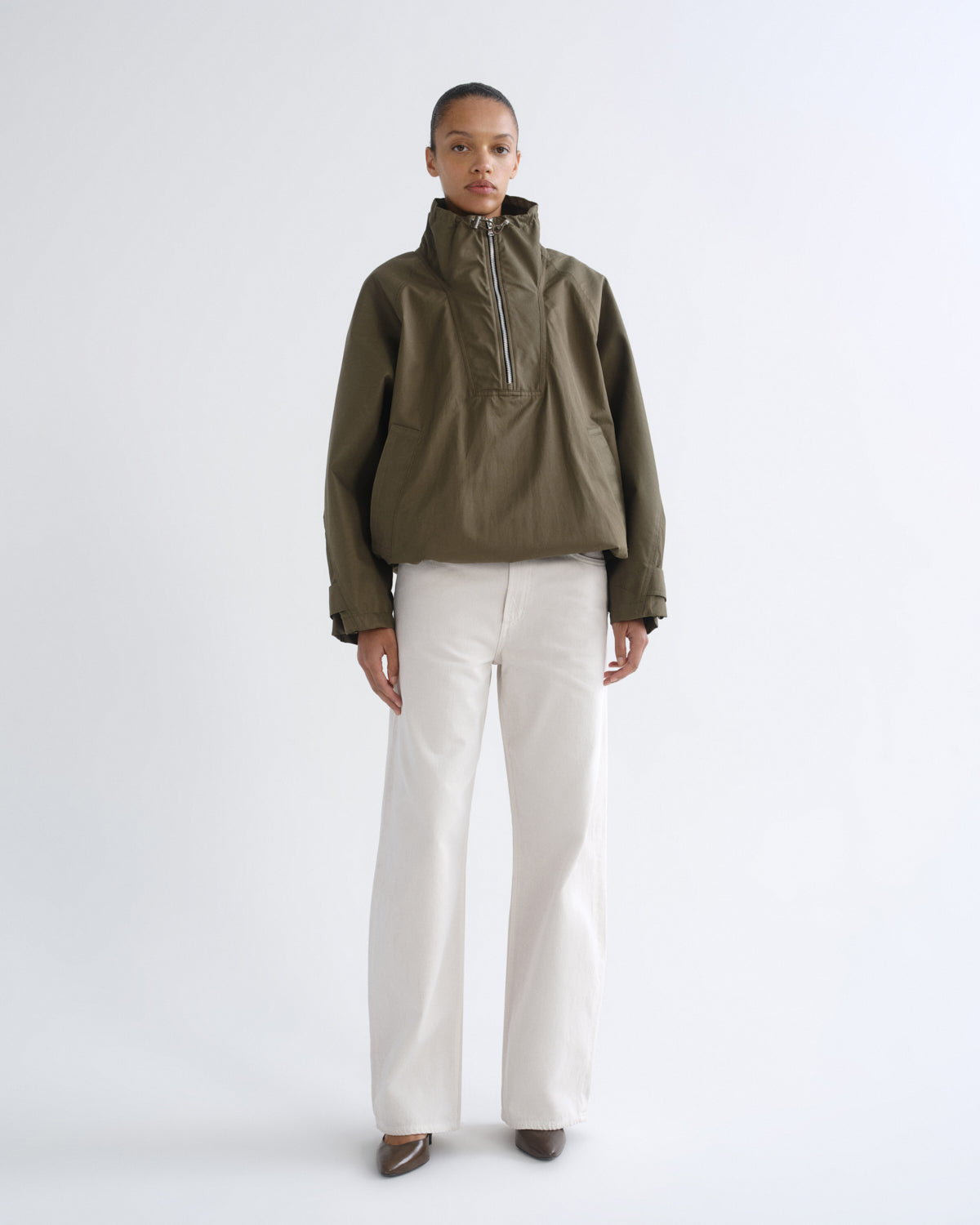Person wearing olive green hooded pullover jacket and white pants, alternate front view