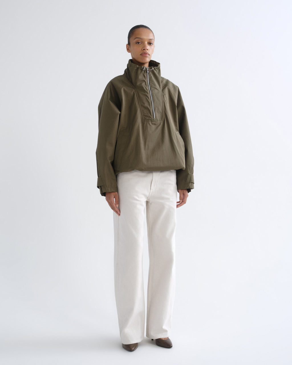 Person wearing olive green hooded pullover jacket and white pants, front view