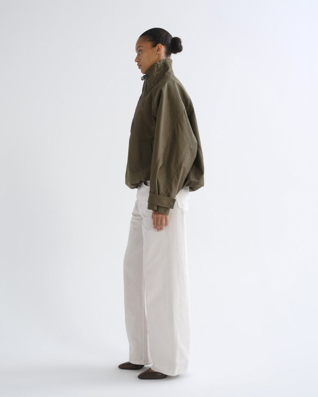 Person wearing olive green hooded pullover jacket and white pants, side view