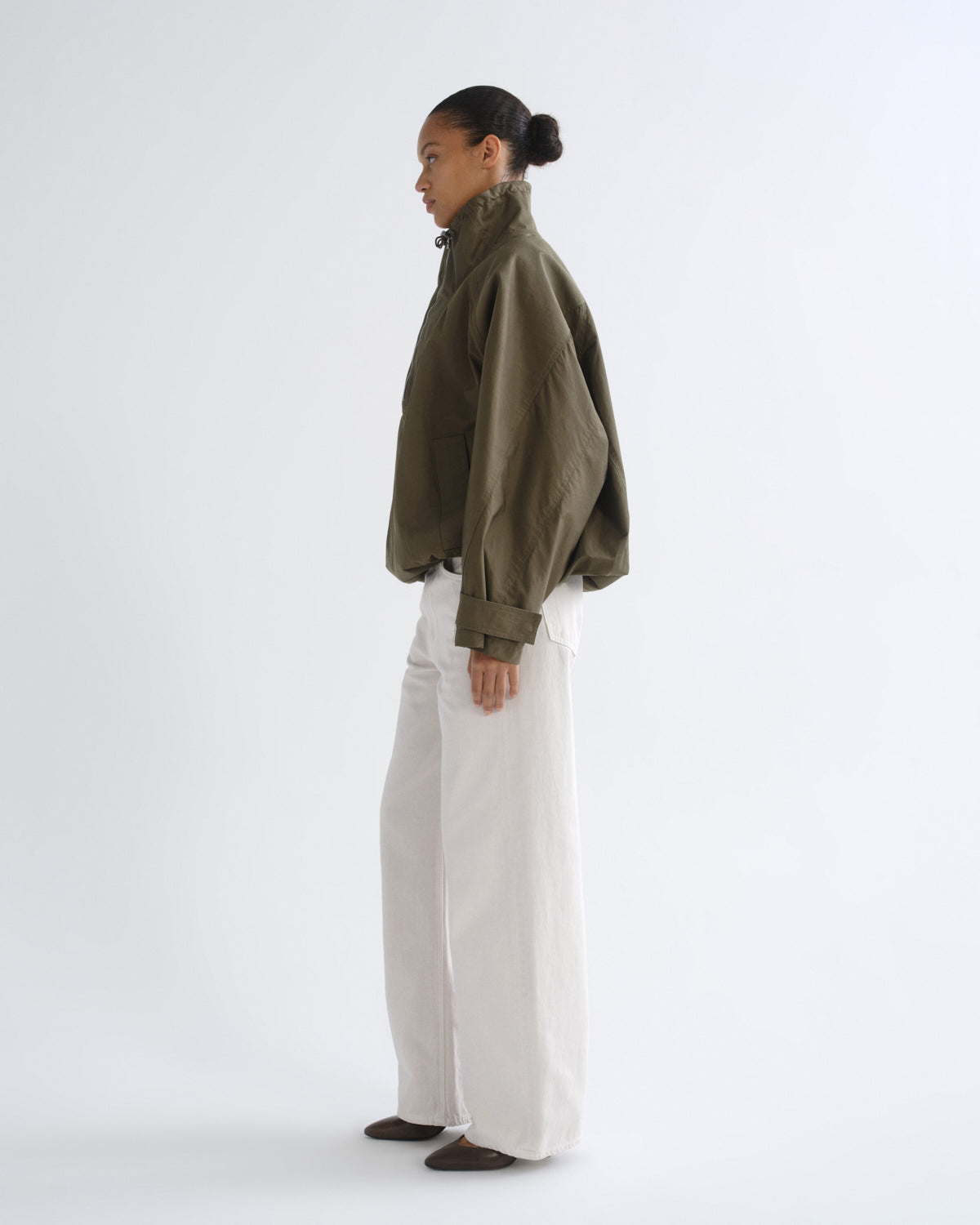 Person wearing olive green hooded pullover jacket and white pants, side view