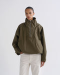 Person wearing olive green hooded pullover jacket and white pants, front crop view