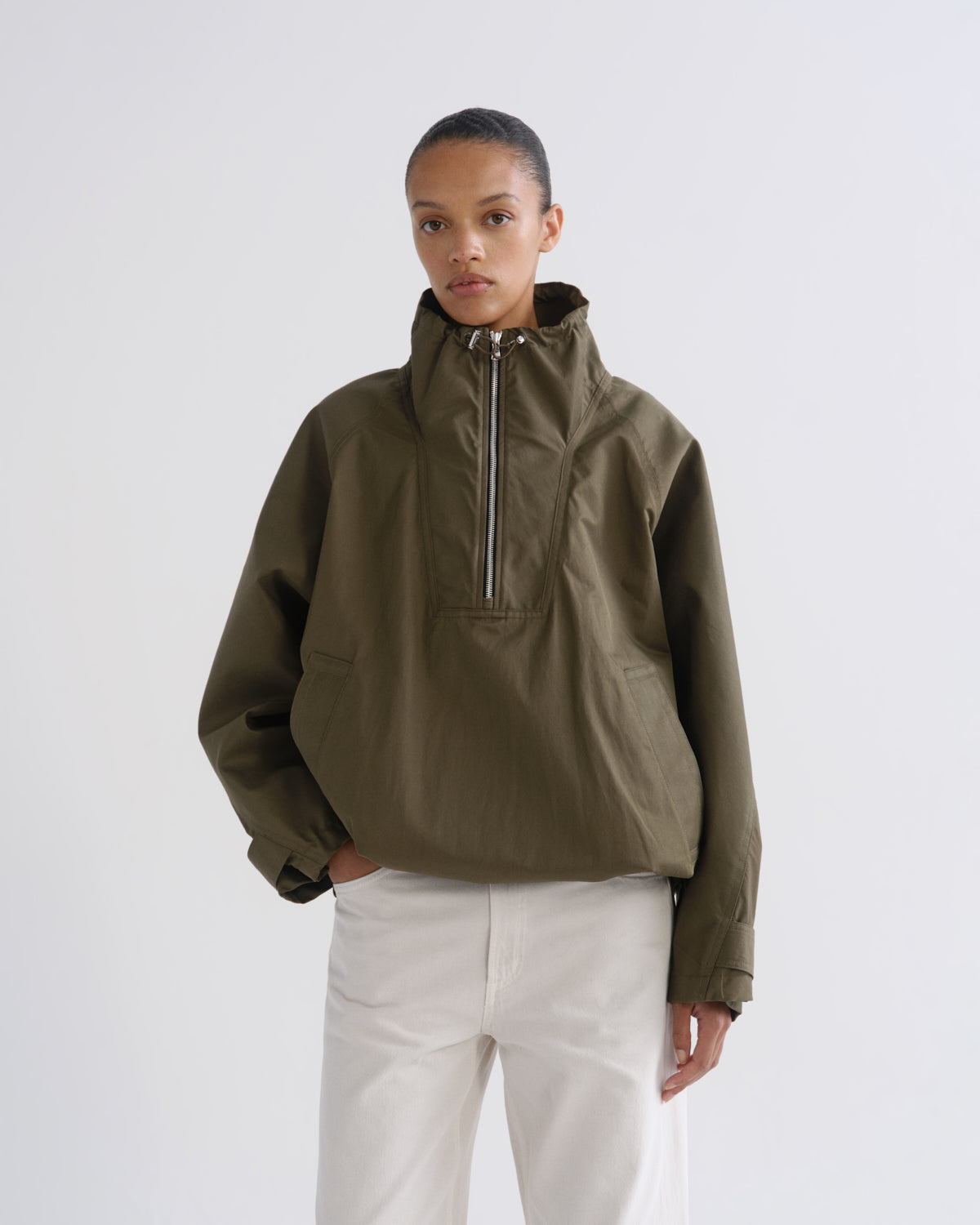 Person wearing olive green hooded pullover jacket and white pants, front crop view