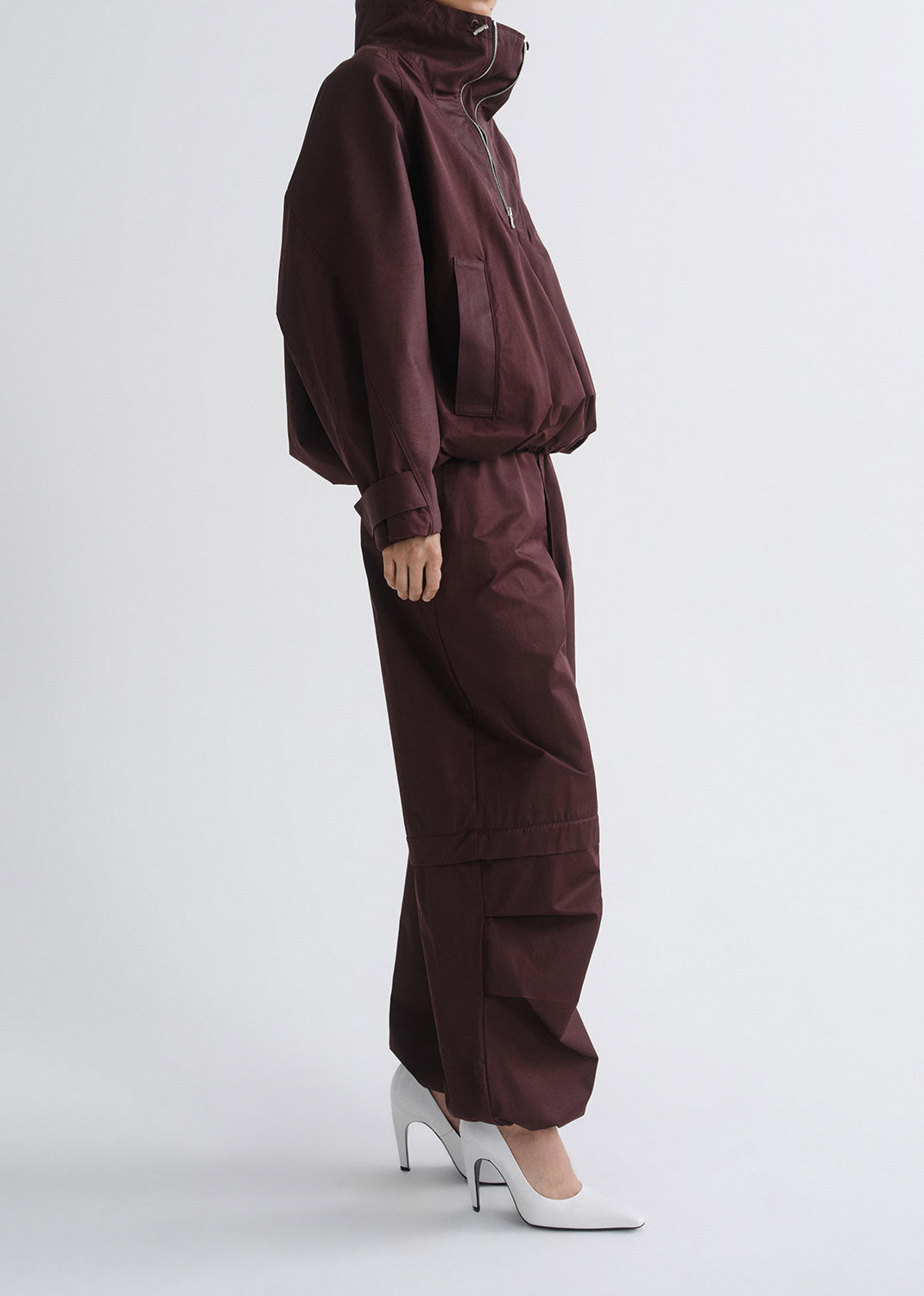 Person wearing a maroon tracksuit with white shoes on a grey background