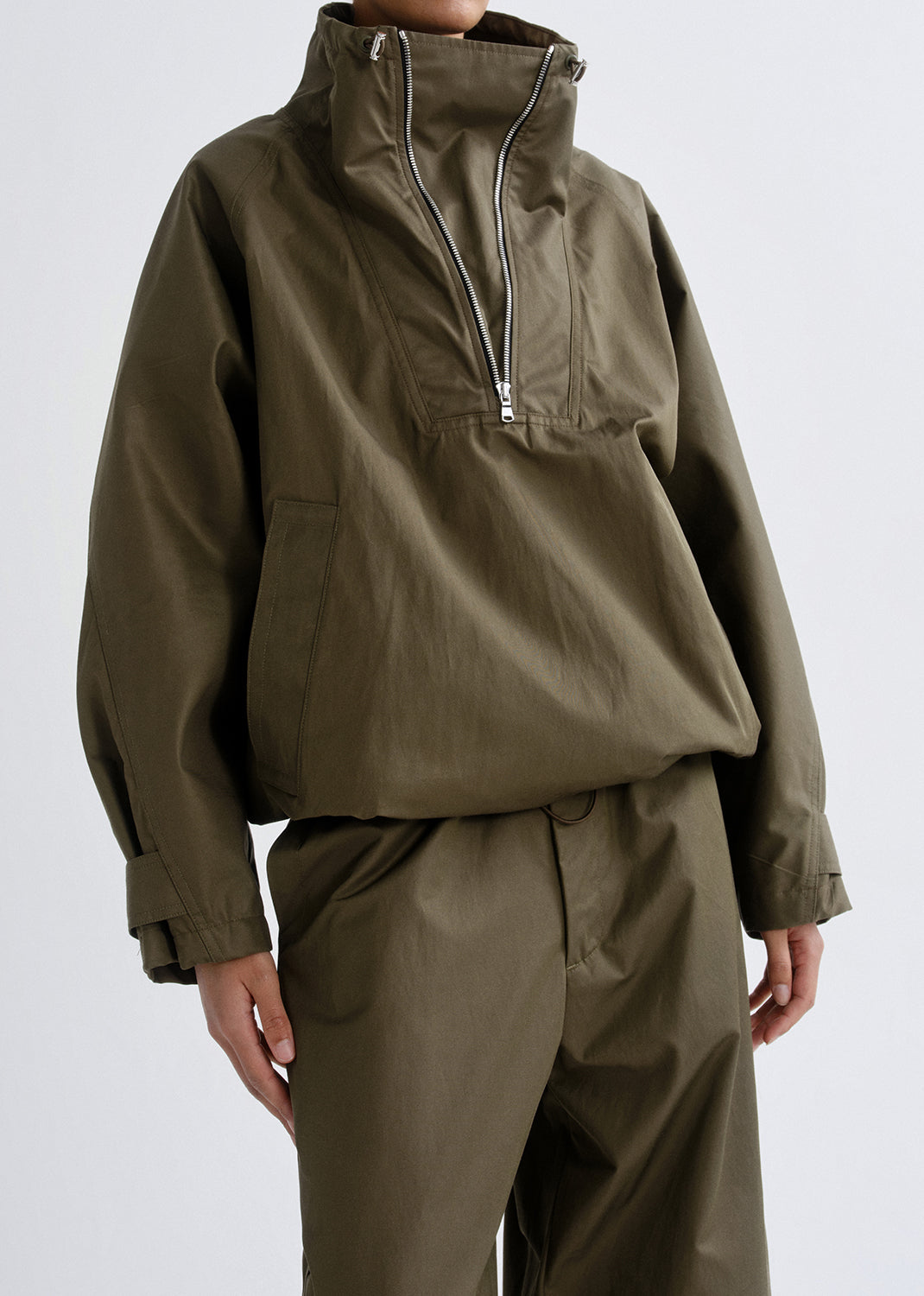 Person wearing a green raincoat and pants on a grey background