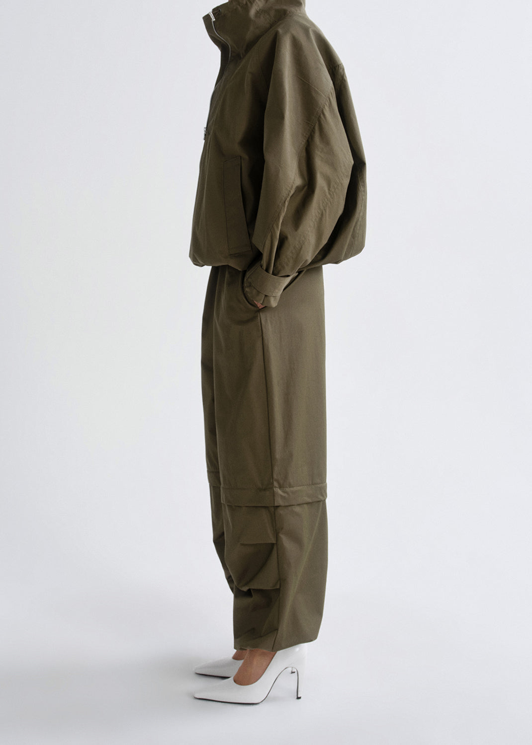 Person wearing a green tracksuit with white shoes on a grey background