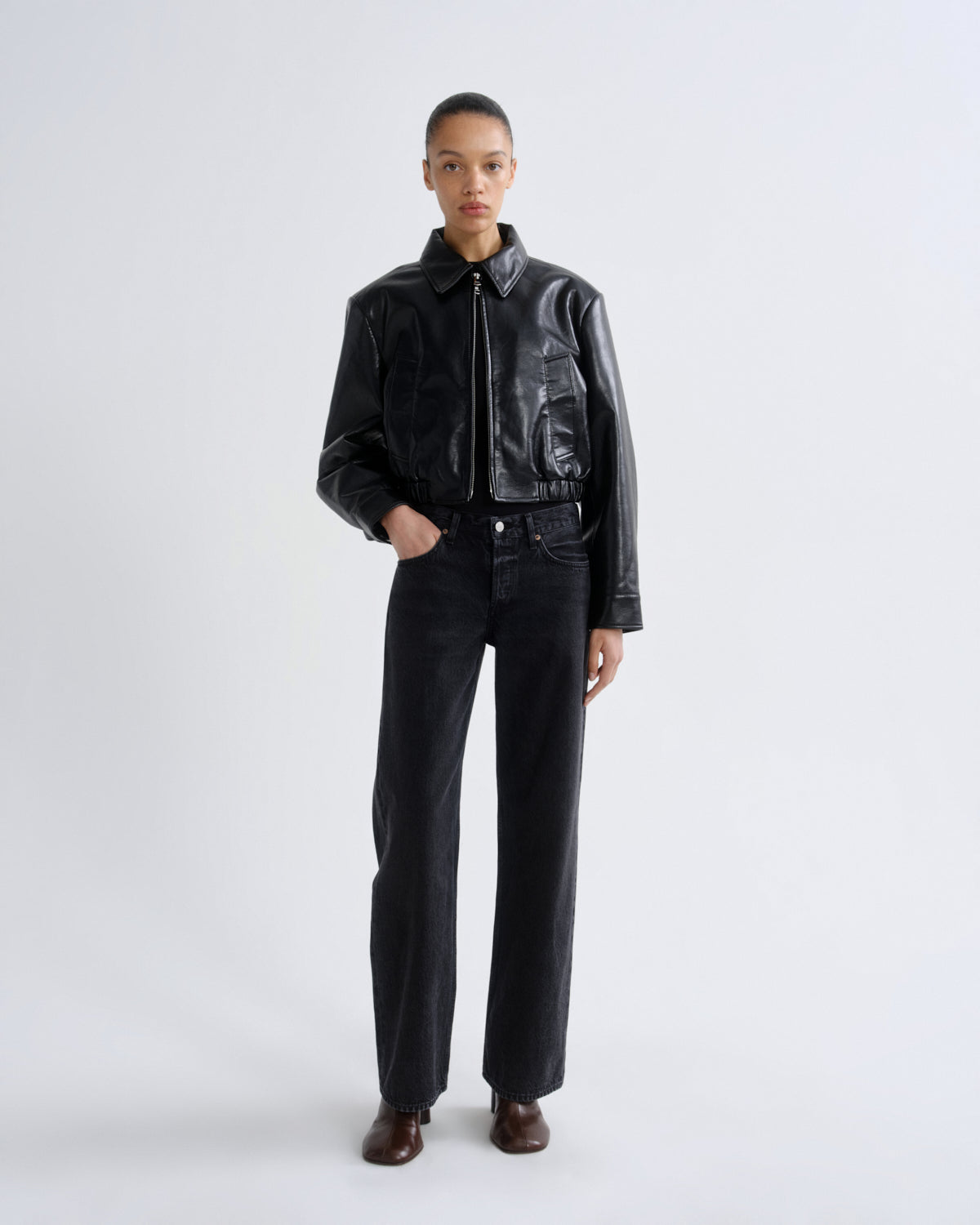 Person wearing a black leather jacket and pants on a white background