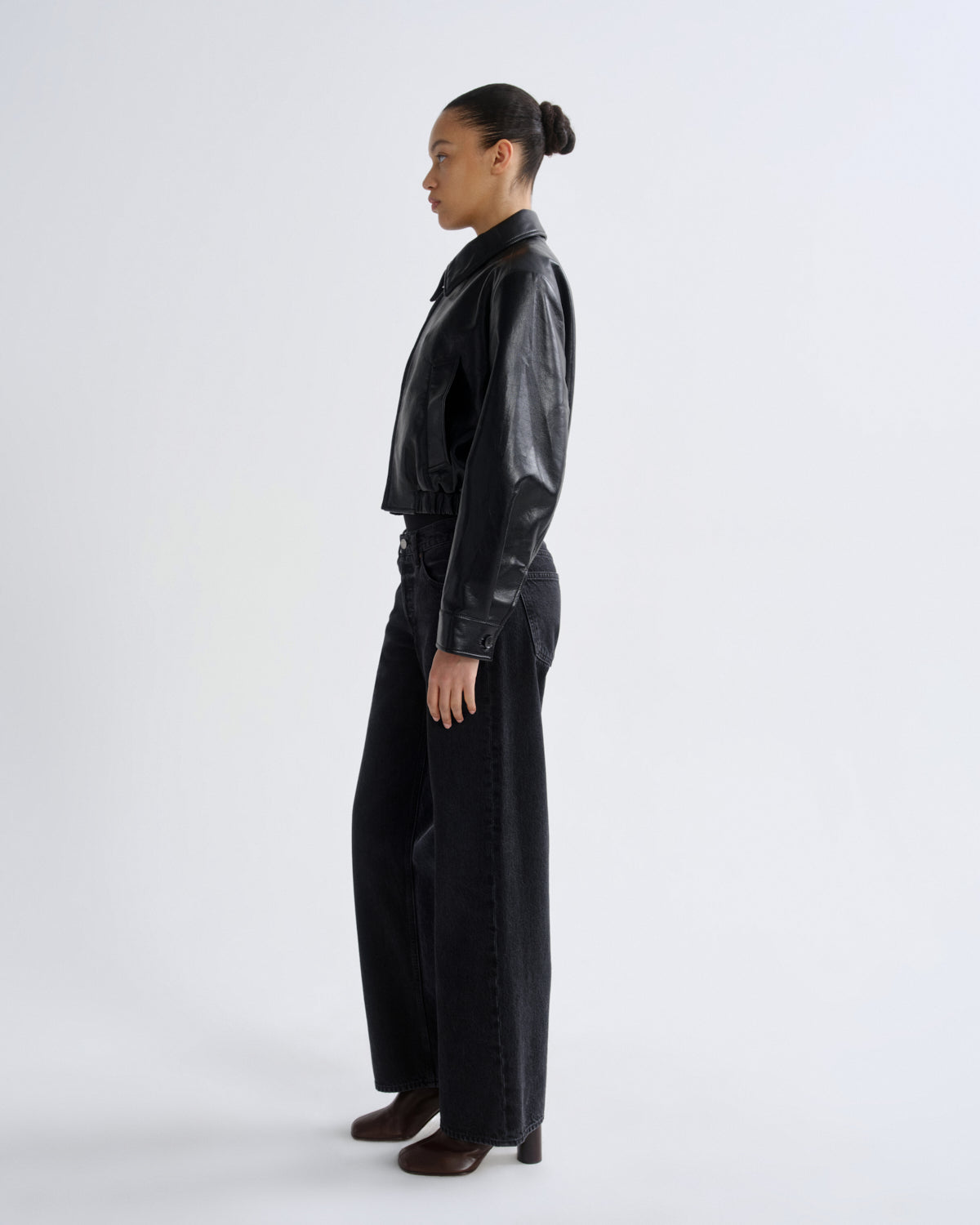 Person wearing a black leather jacket and pants on a white background
