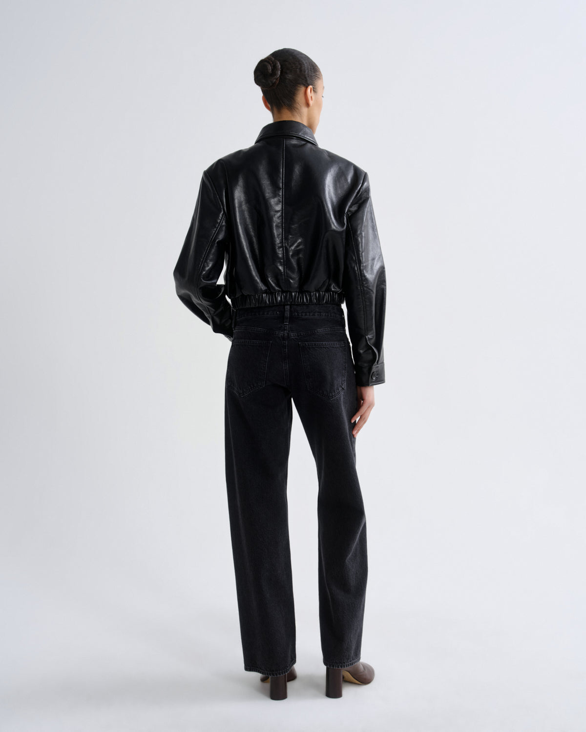 Person wearing a black leather jacket and pants on a white background