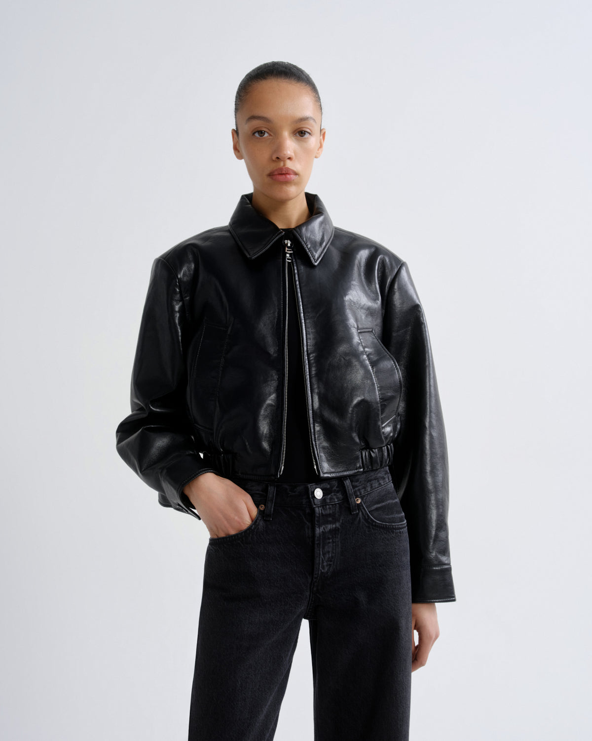Person wearing a black leather jacket and black pants on a white background