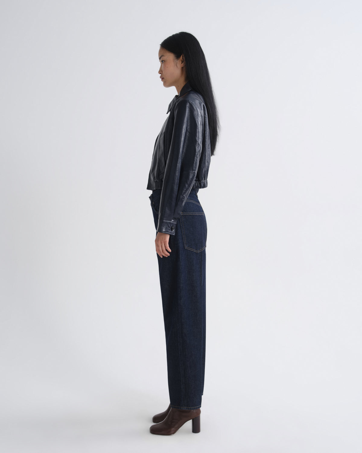 Person wearing a dark shirt and jeans standing against a white background