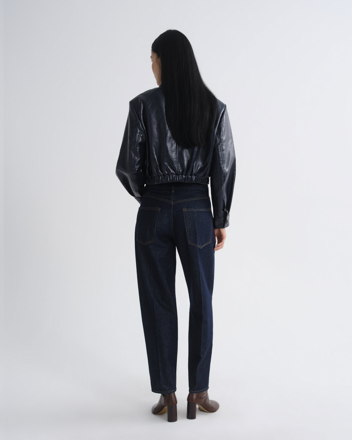Person wearing a black leather jacket and dark jeans on a white background
