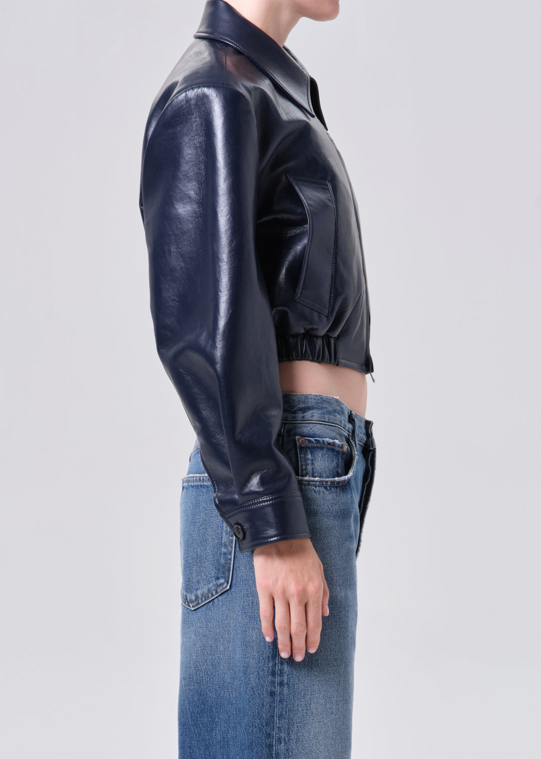 Person wearing a navy leather jacket and blue jeans on a light gray background
