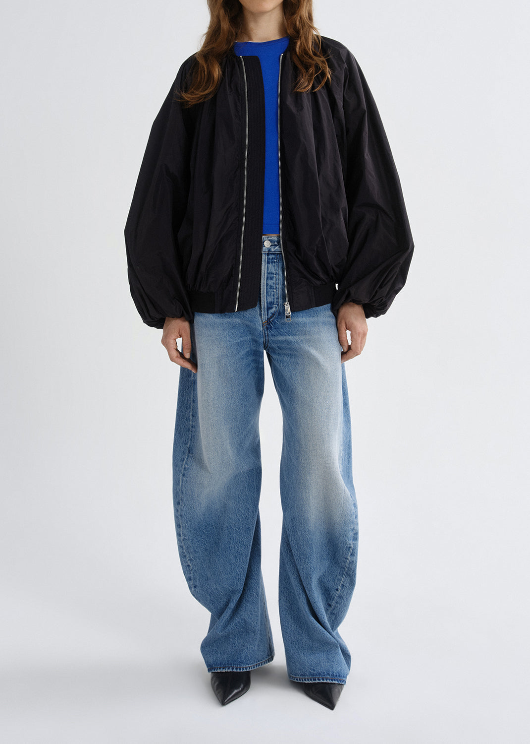 Person wearing a black jacket and blue jeans on a grey background