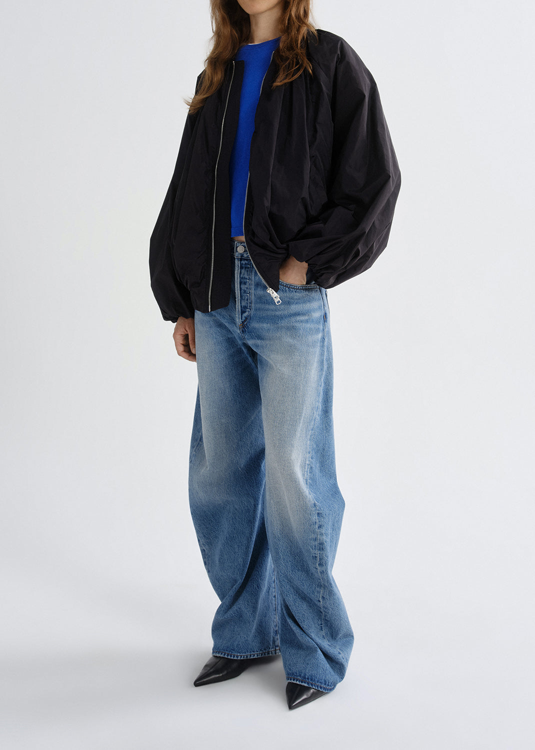 Person wearing a black jacket, blue shirt, and jeans on a grey background