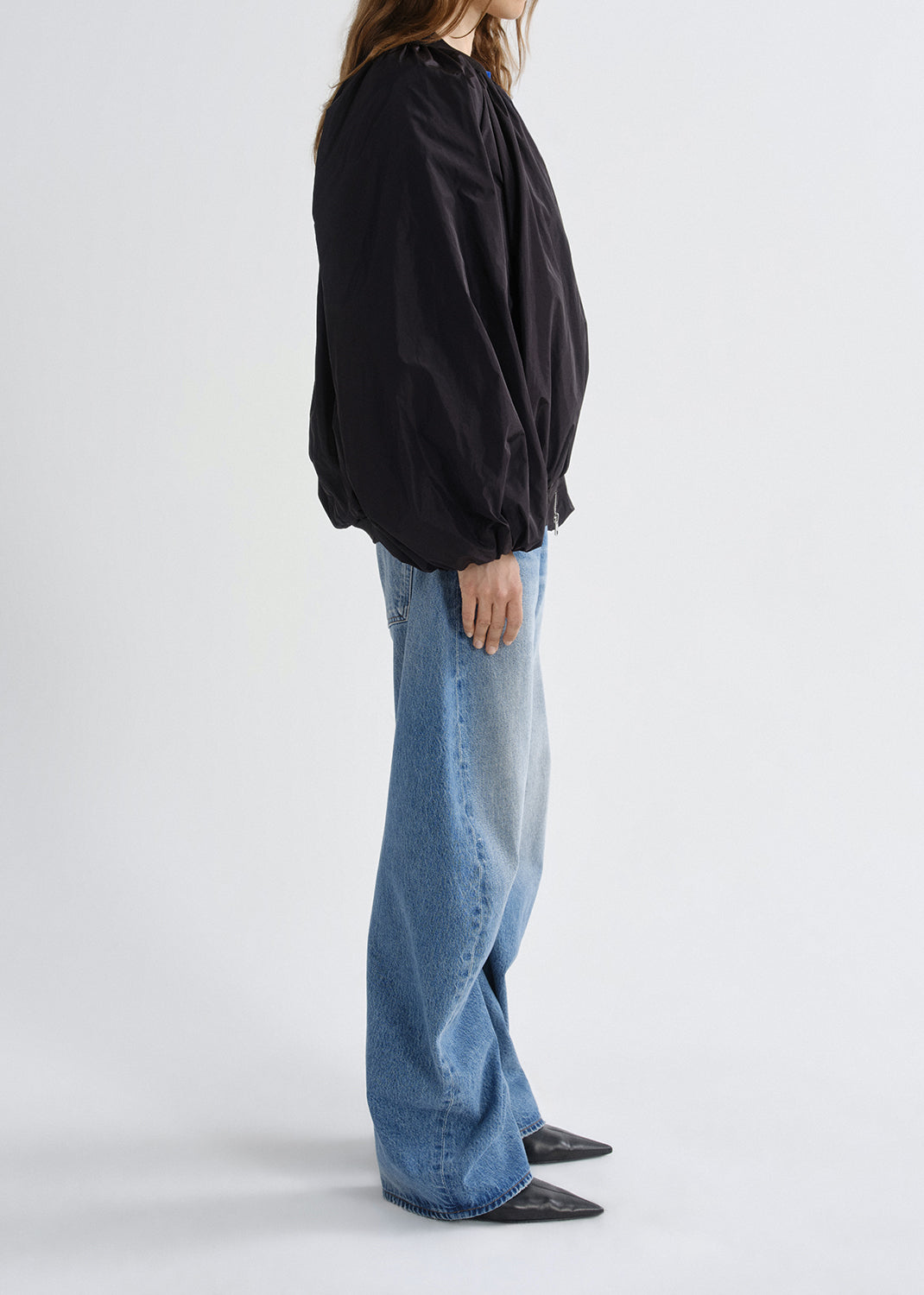 Person wearing a black oversized shirt and blue jeans on a grey background