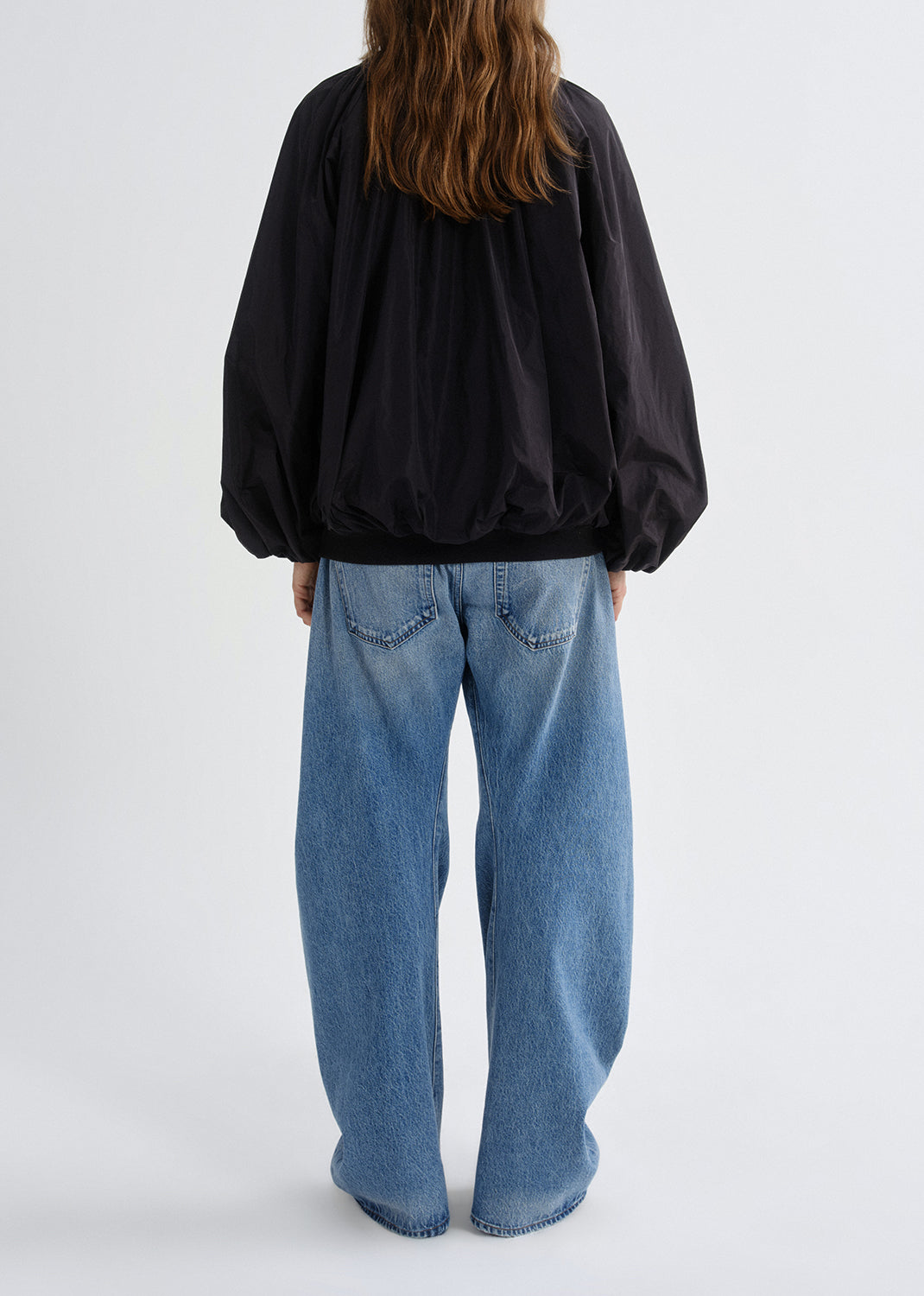 Person wearing a black jacket and blue jeans on a grey background