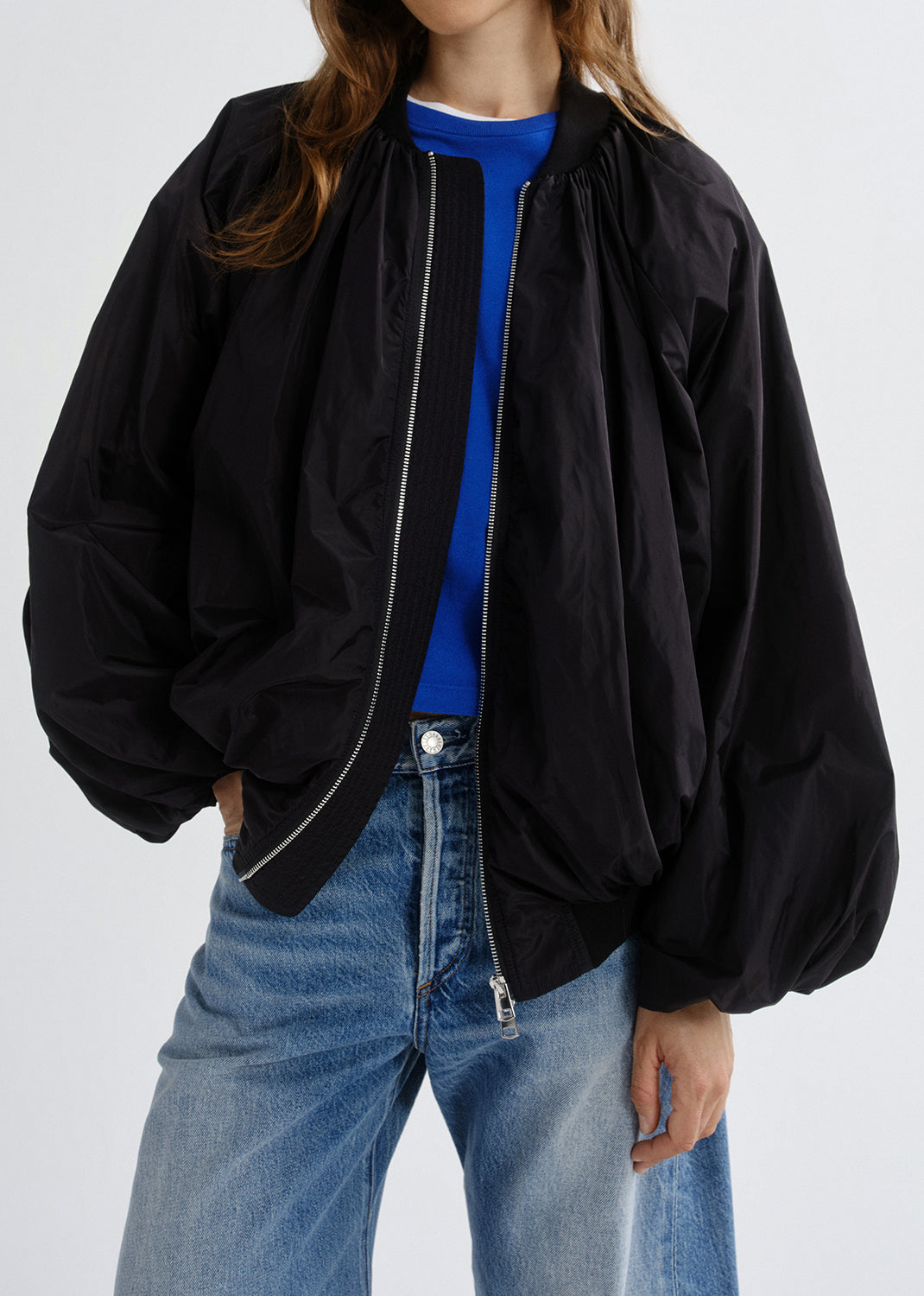 Person wearing a black jacket over a blue shirt and jeans on a grey background