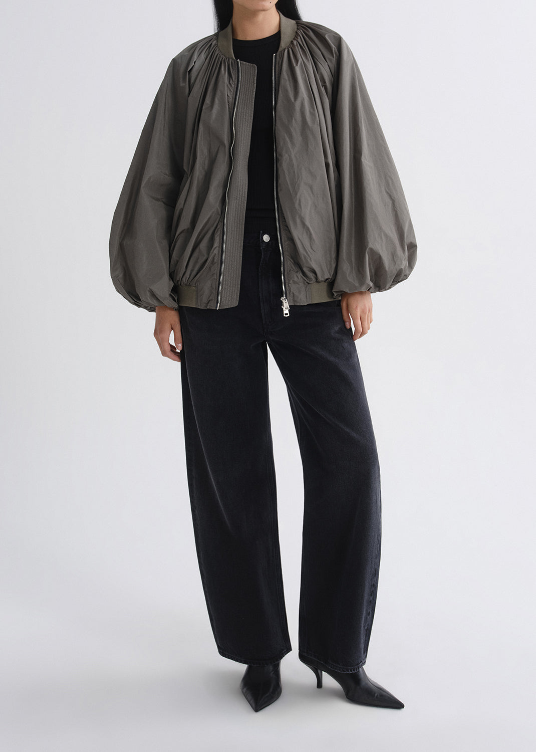 Person wearing a gray jacket and black pants on a grey background