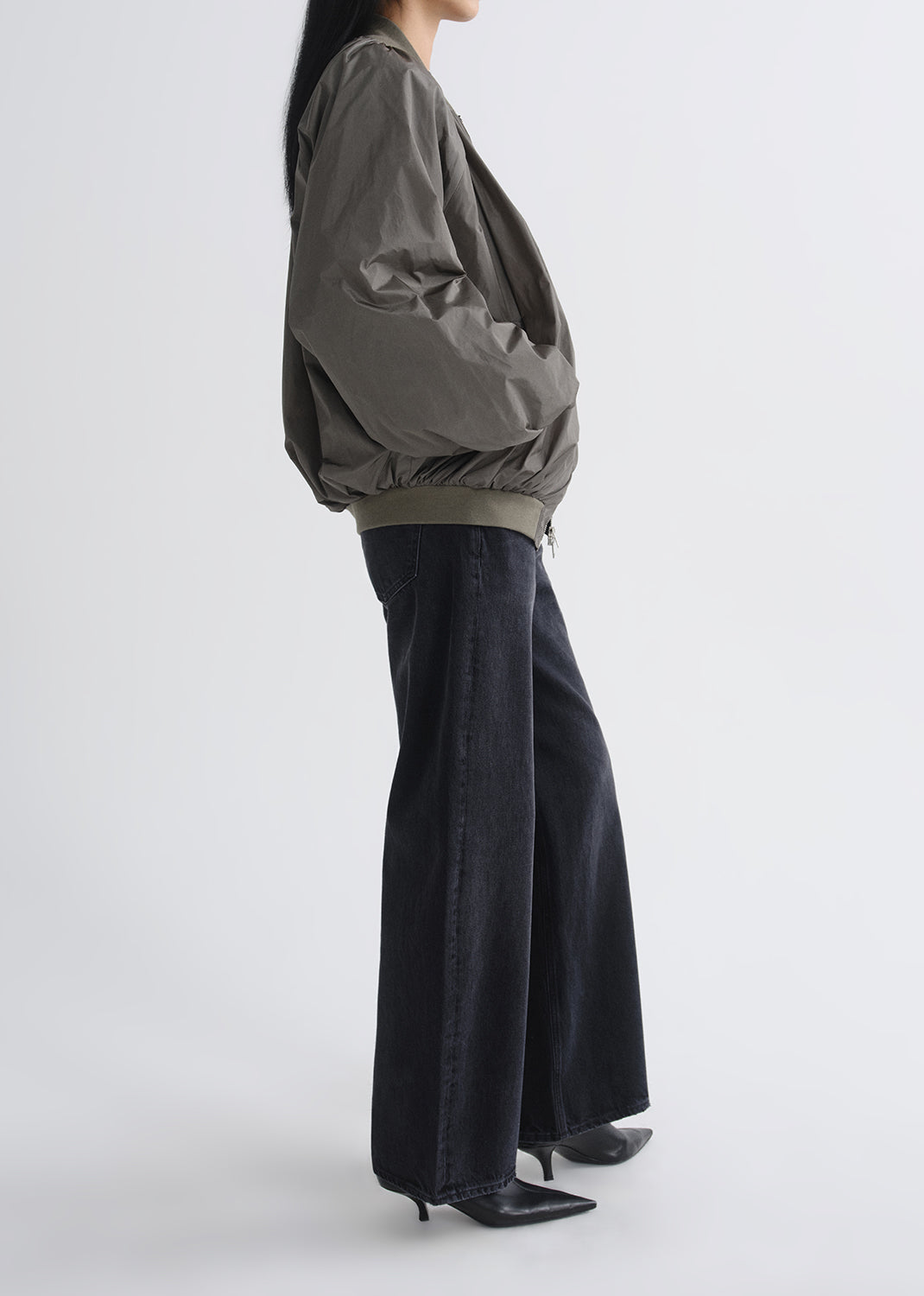 Person wearing a green jacket and black pants on a grey background