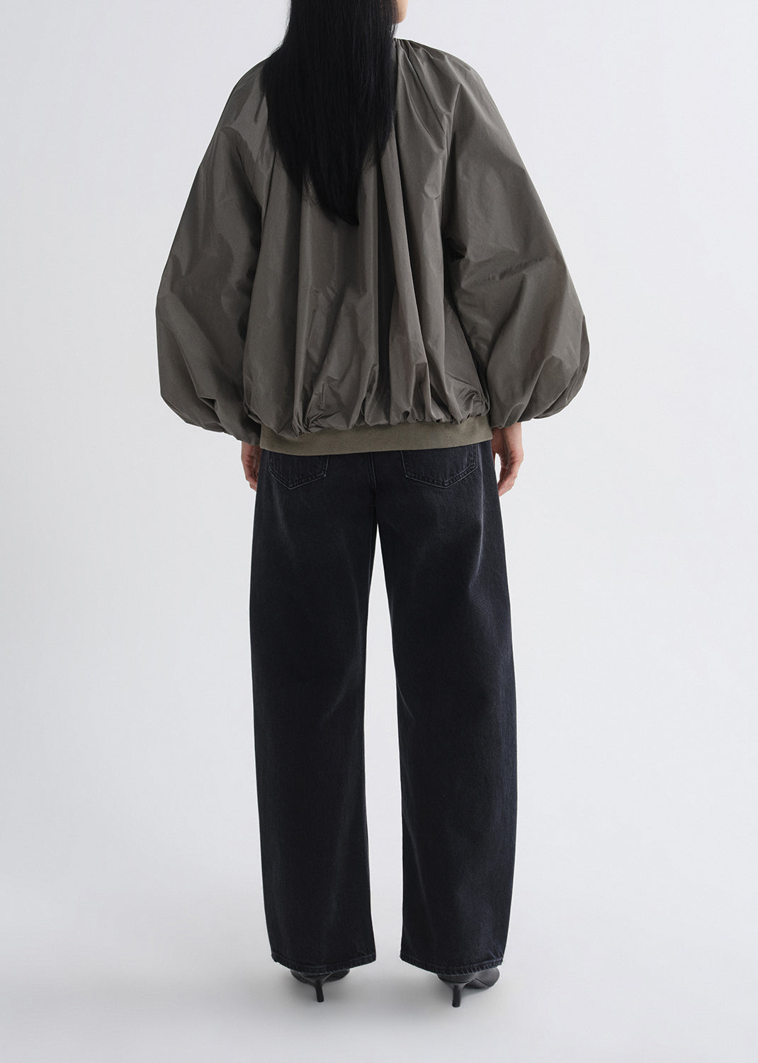 Person wearing a green jacket and black pants on a grey background
