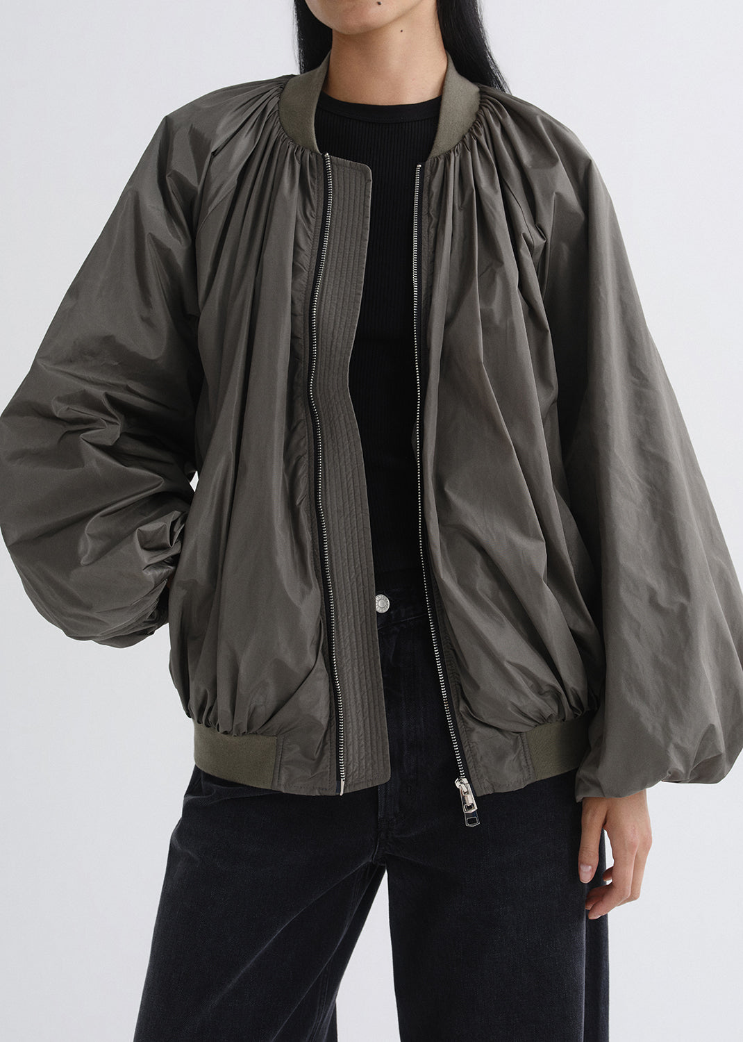 Person wearing a green bomber jacket on a grey background