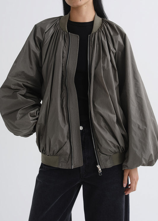 Person wearing a green bomber jacket on a grey background