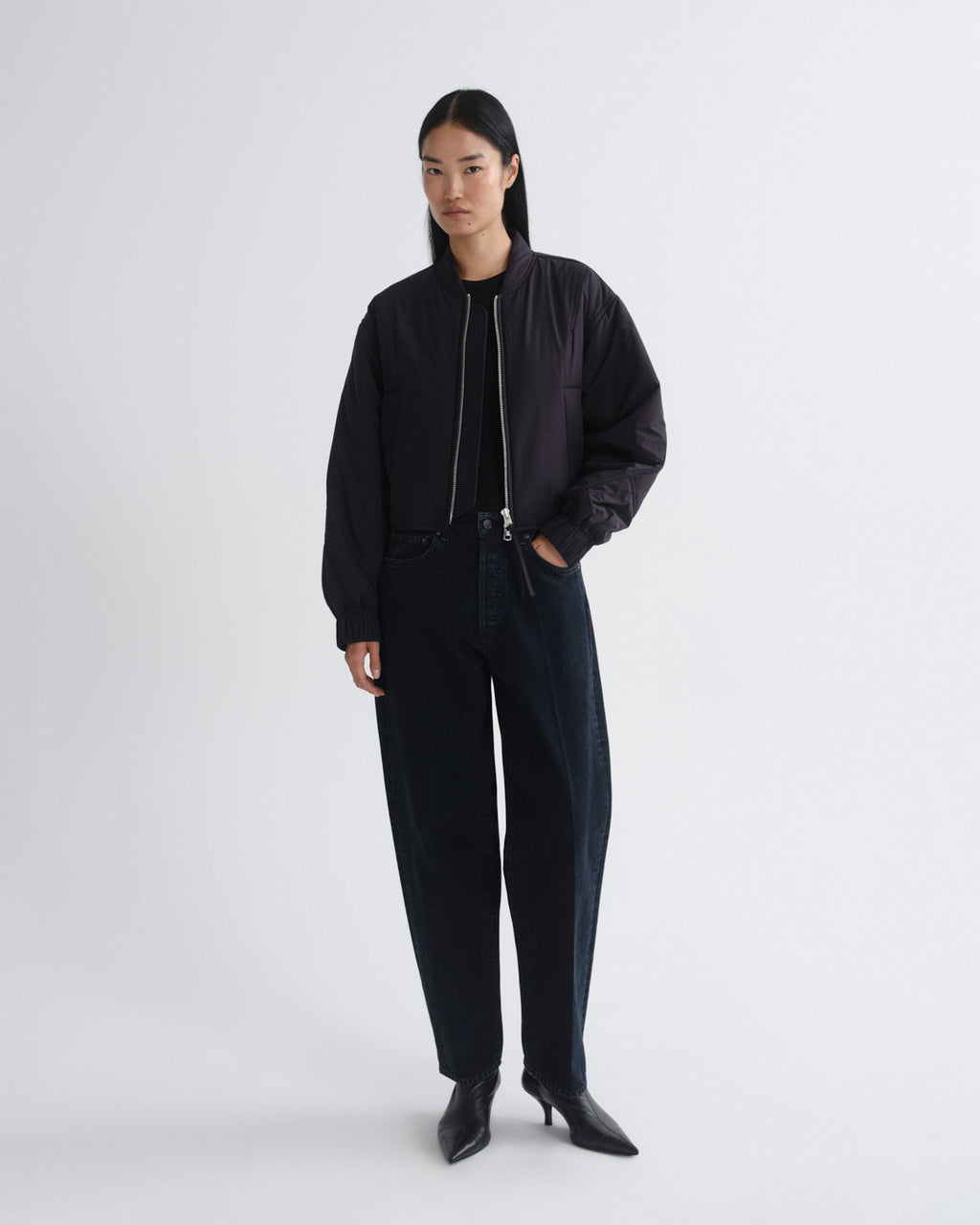 Person wearing a black bomber jacket and pants on a white background