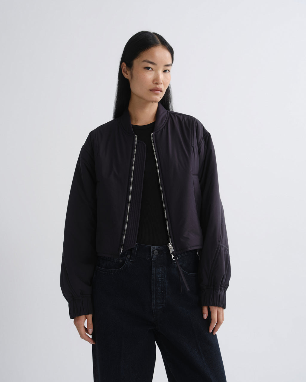 Person wearing a black bomber jacket and pants on a white background