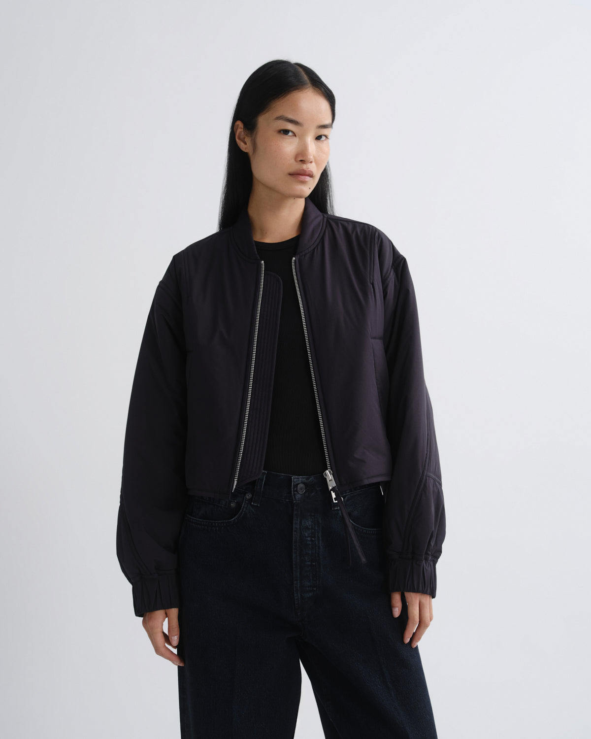 Person wearing a black bomber jacket and pants on a white background