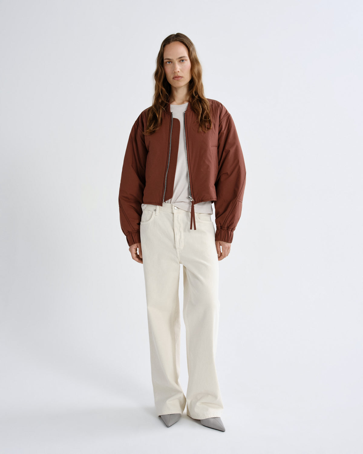 Person wearing a brown jacket and white pants on a white background