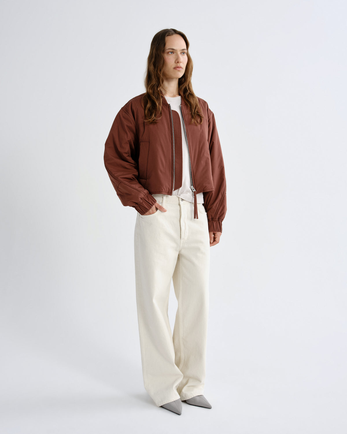 Person wearing a brown jacket and white pants on a plain background