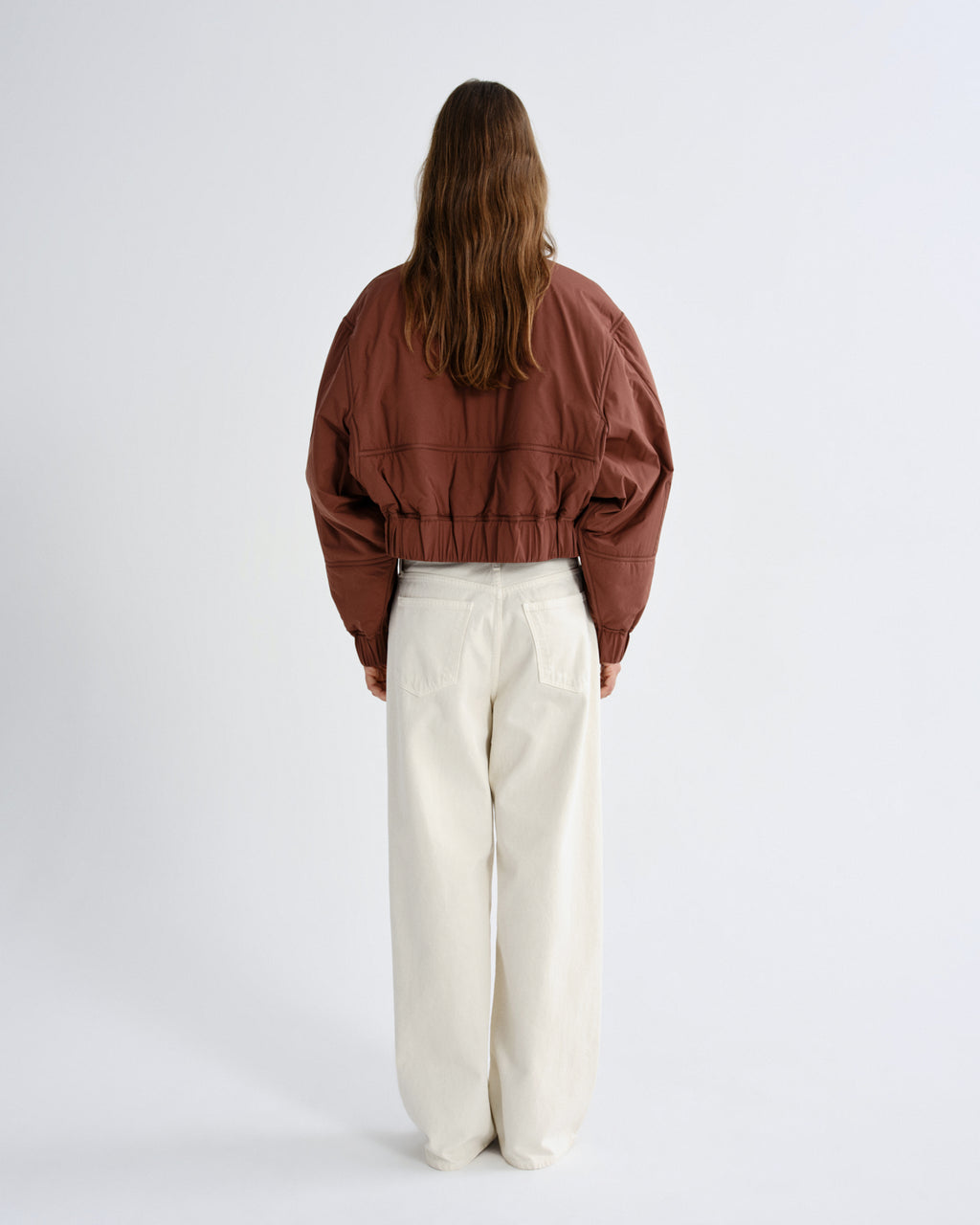 Person wearing a brown jacket and white pants on a white background