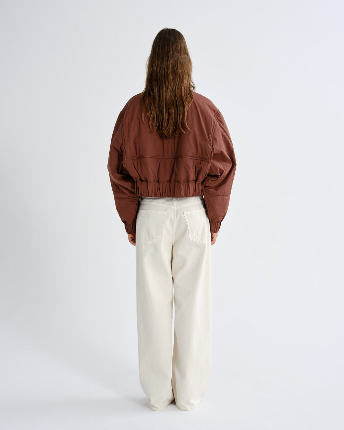 Person wearing a brown jacket and white pants on a white background