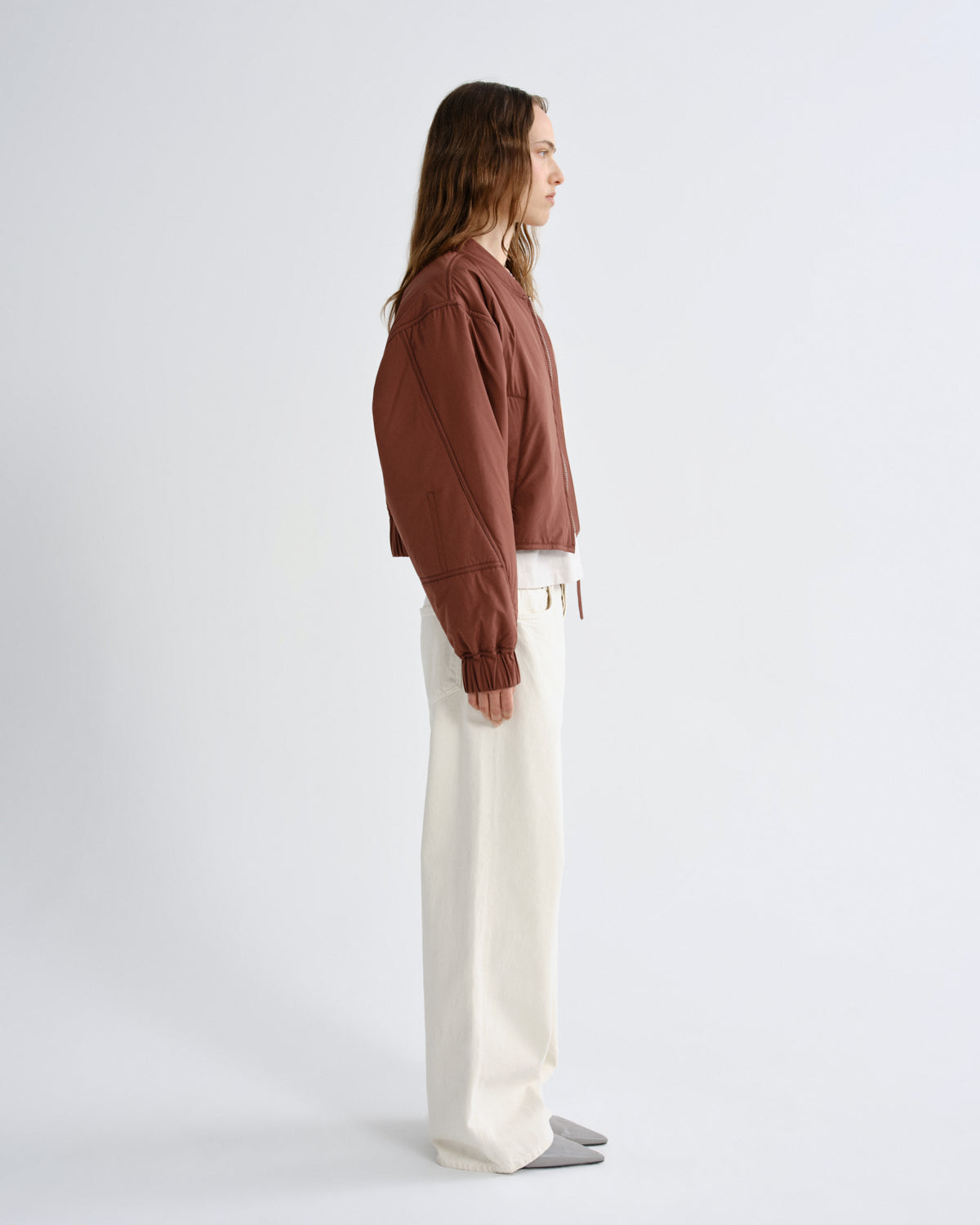 Person wearing a brown shirt and white pants on a light gray background
