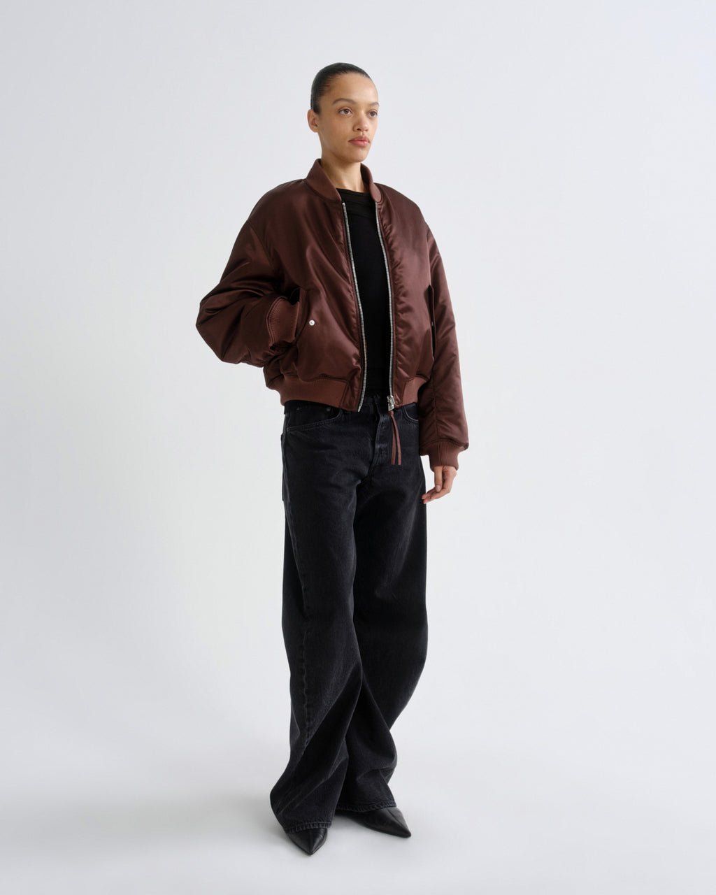 Person wearing a brown red bomber jacket and black pants on a grey background