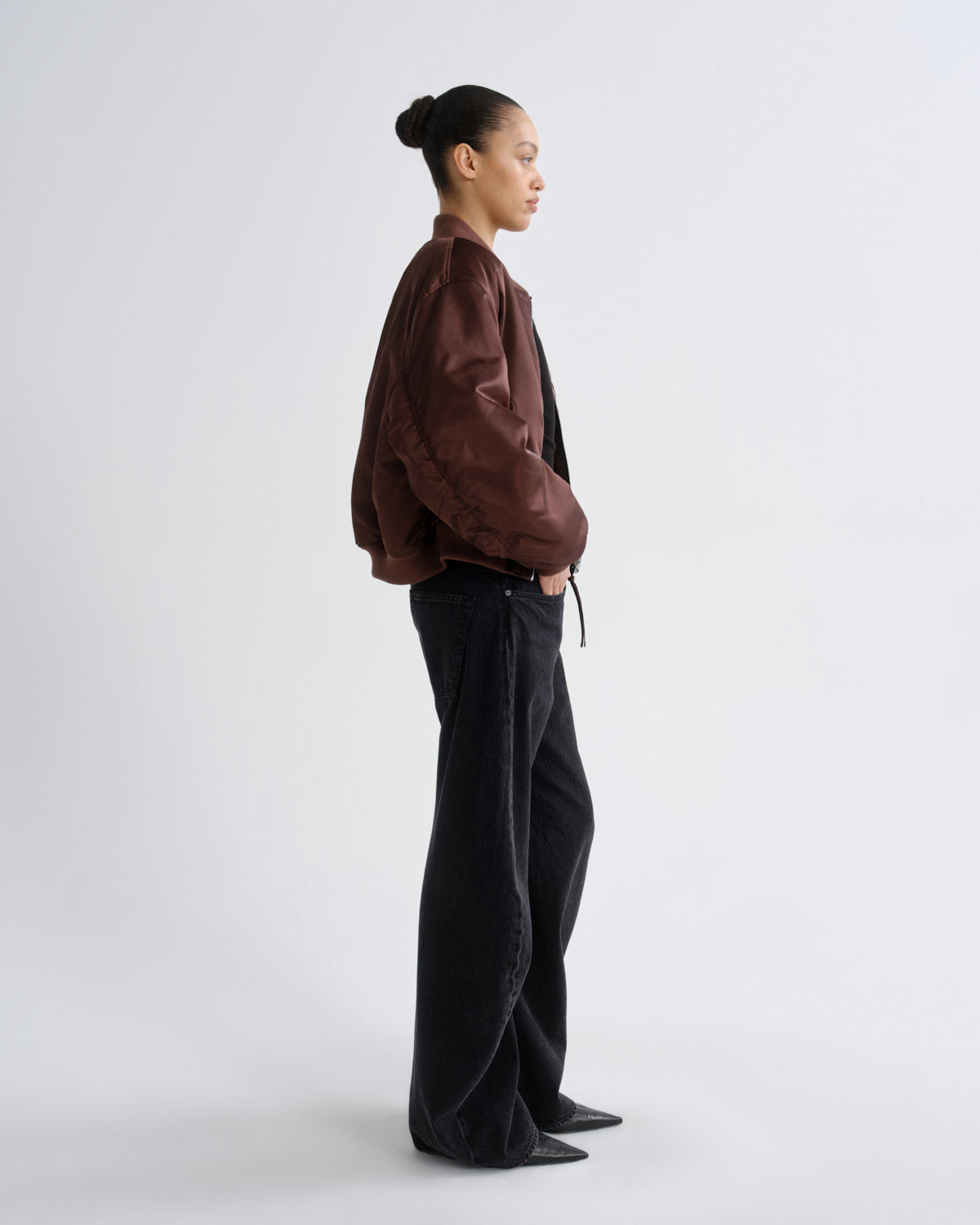 Person wearing a brown red bomber jacket and black pants on a grey background