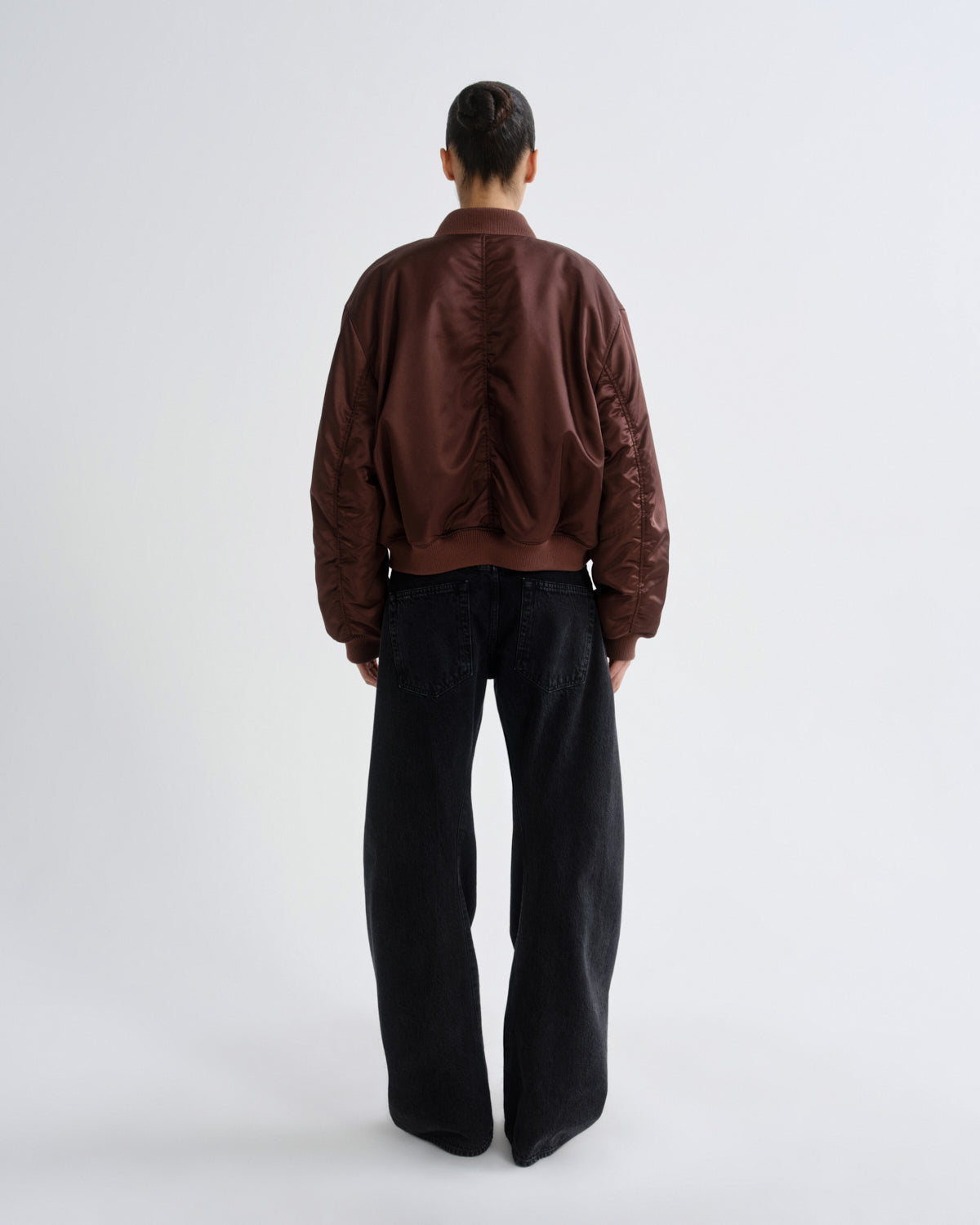 Person wearing a brown red bomber jacket and black pants on a grey background