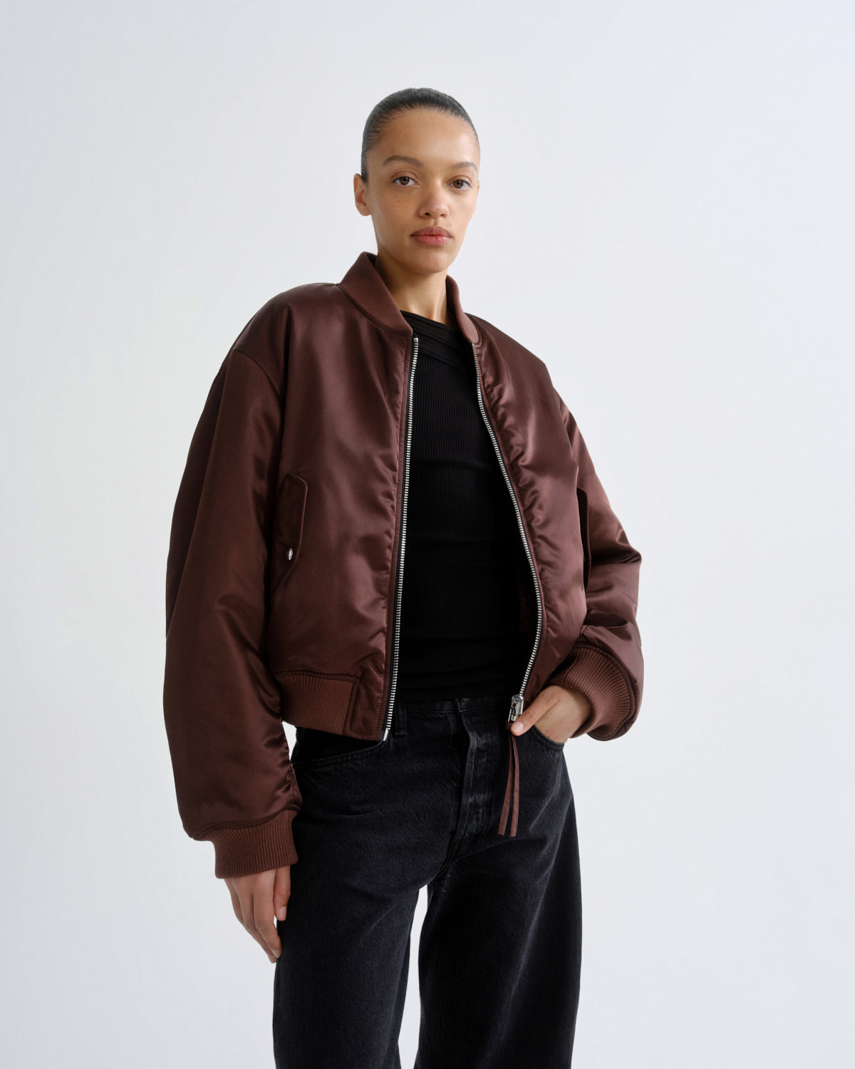 Close up of person wearing red brown bomber jacket with black pants on a grey background