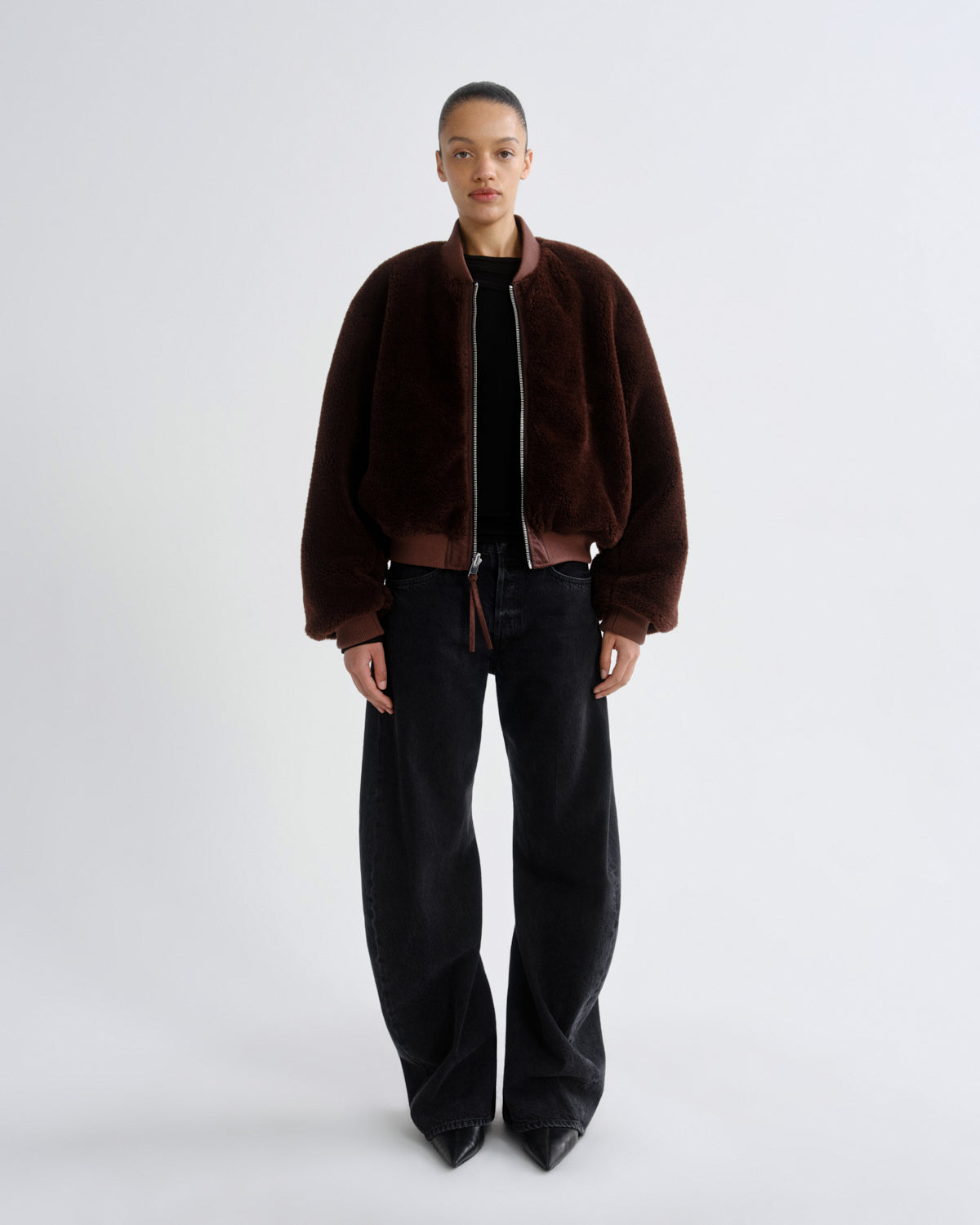 Person wearing a brown red reversible bomber jacket and black pants on a grey background