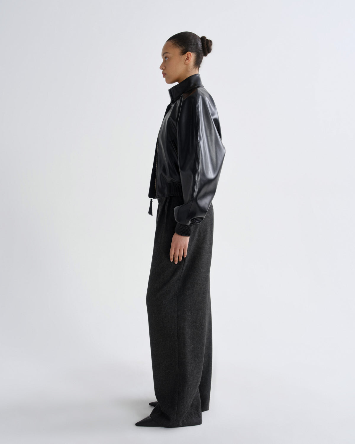 Person wearing a black outfit with a high collar and wide-leg pants on a white background