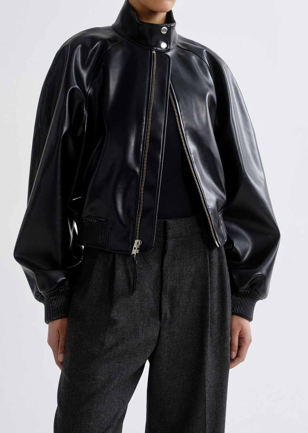 Person wearing a black leather bomber jacket on a grey background.