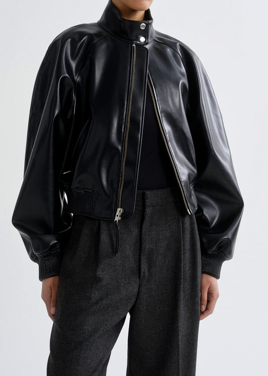 Person wearing a black leather bomber jacket on a grey background.