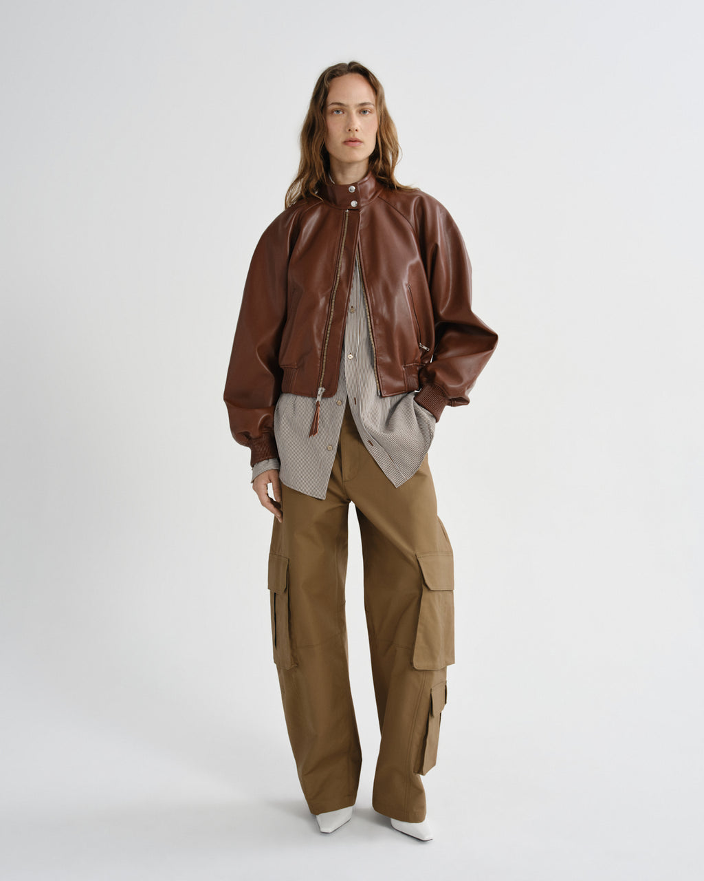 Person wearing a brown leather jacket and tan cargo pants on a white background