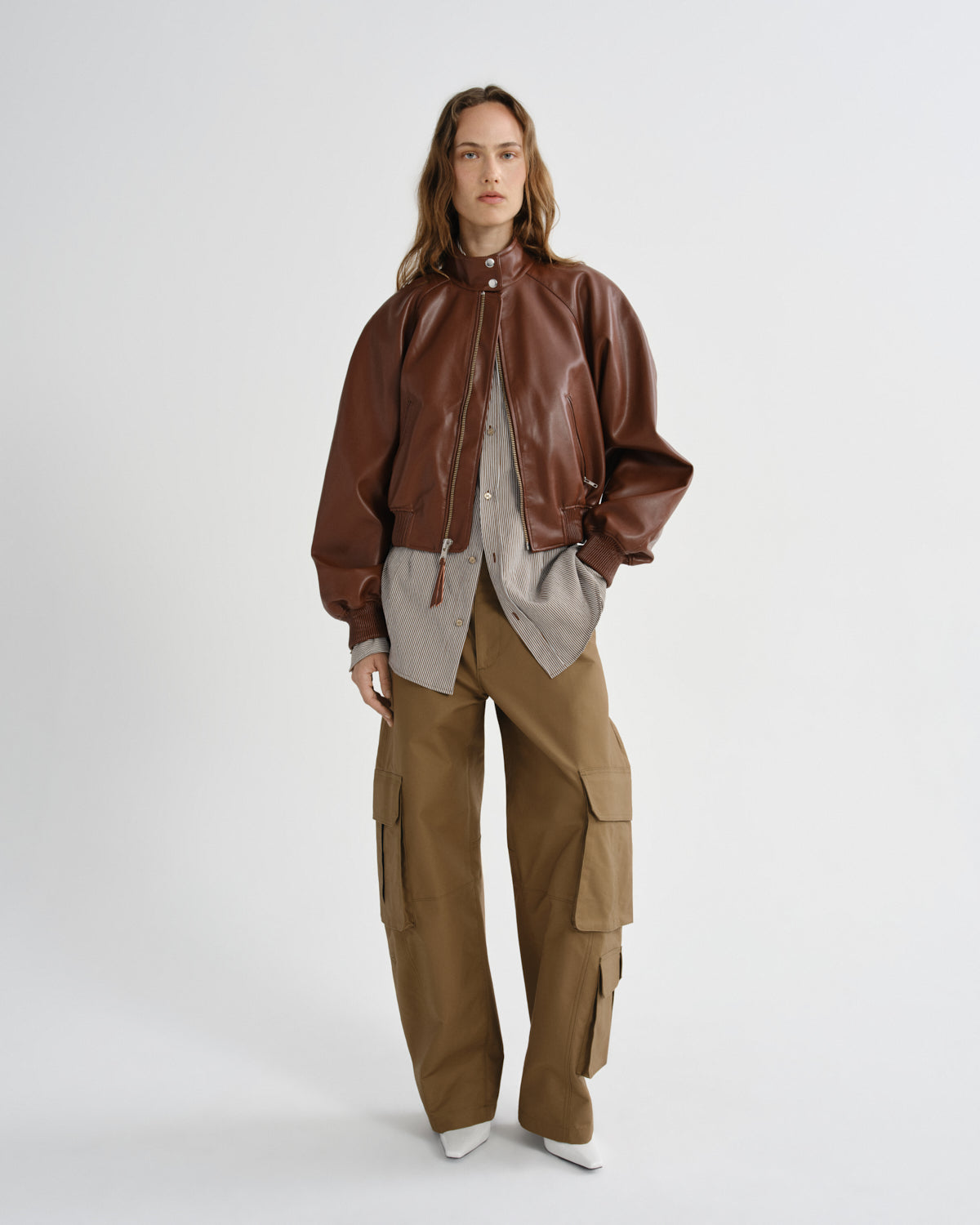 Person wearing a brown leather jacket and tan cargo pants on a white background
